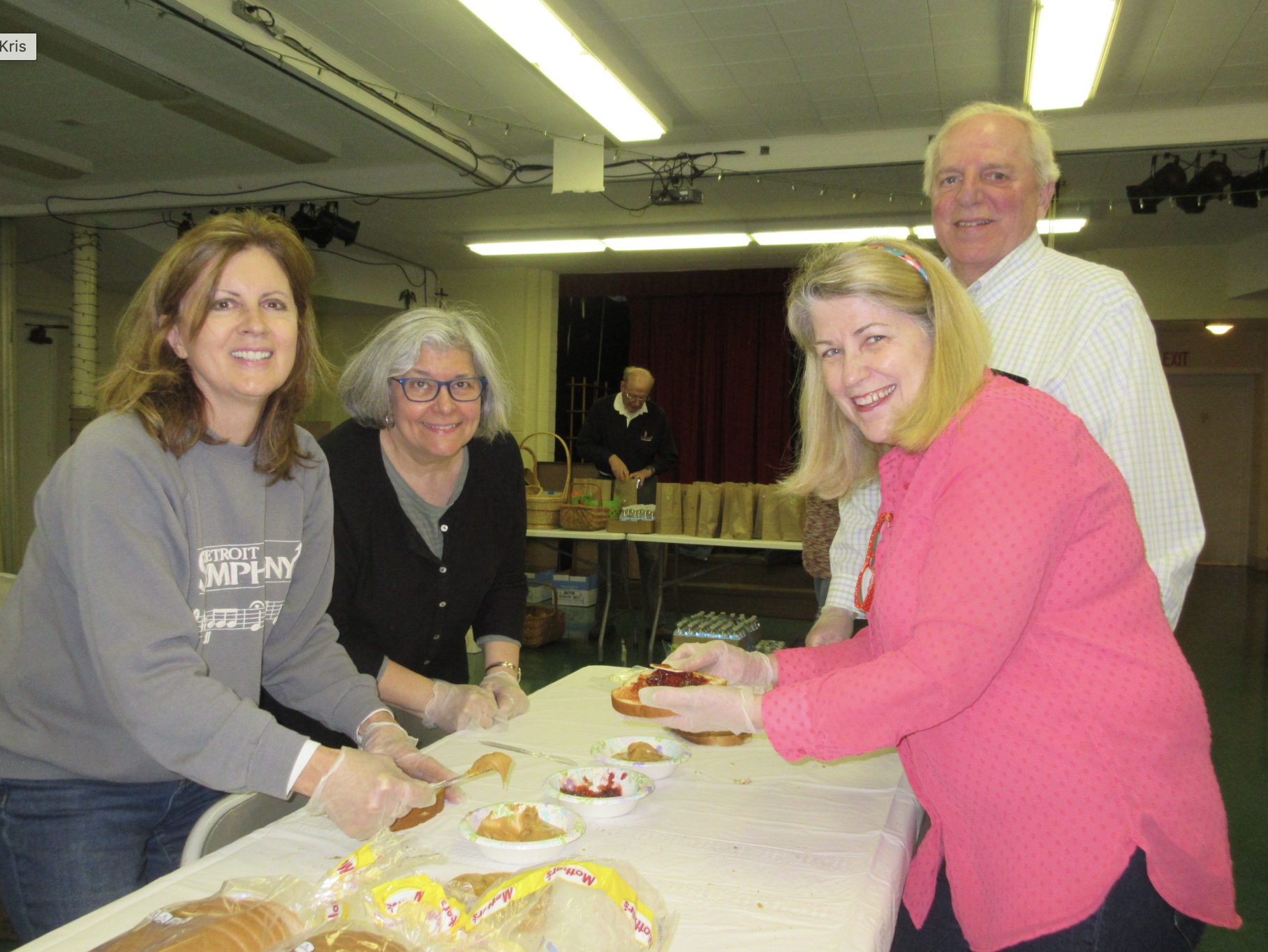 People preparing sandwiches at a community event, with tables filled with bread and spreads.