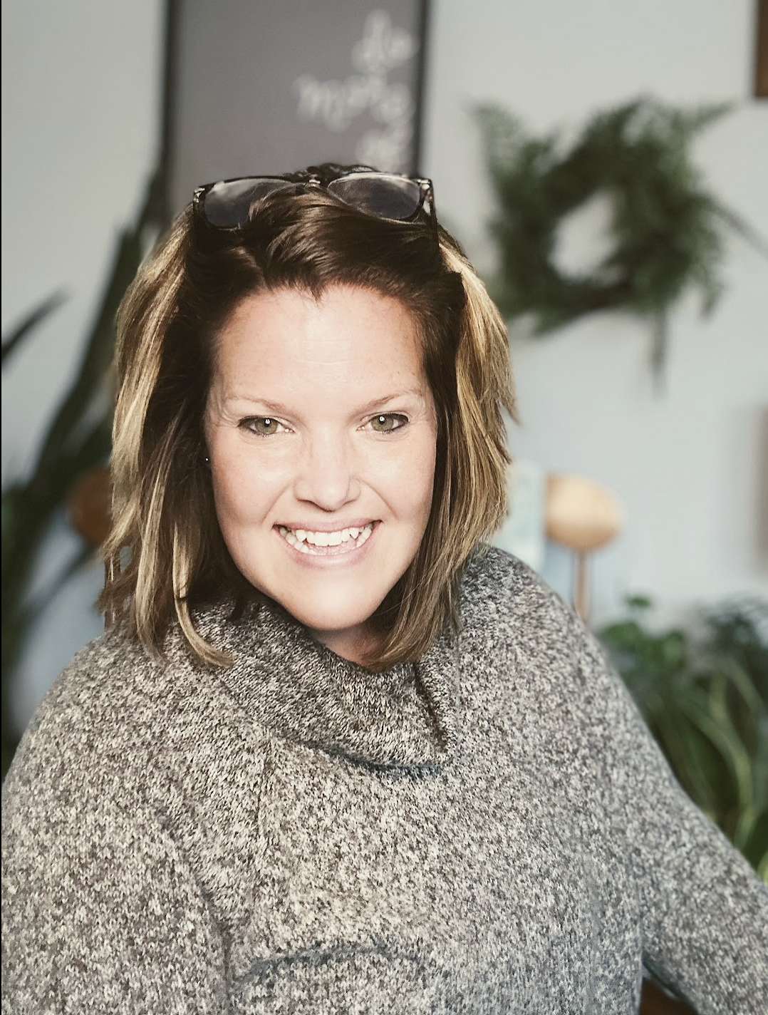 Image of a woman sitting on a couch, smiling, with dark hair, wearing a black sweater and white pants.