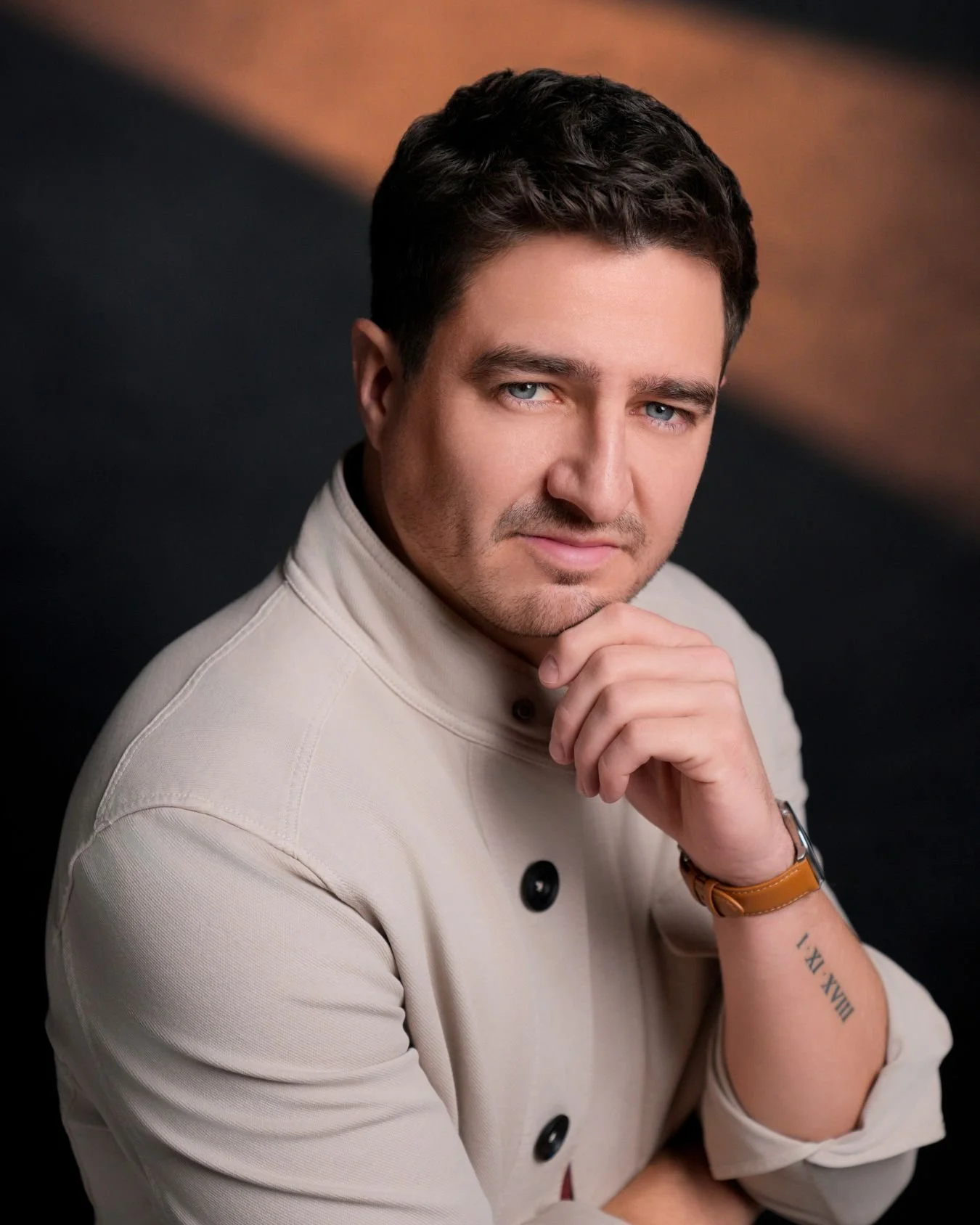Executive headshot of a man in a beige jacket with hand on chin, warm-toned corporate portrait taken in Minneapolis studio.