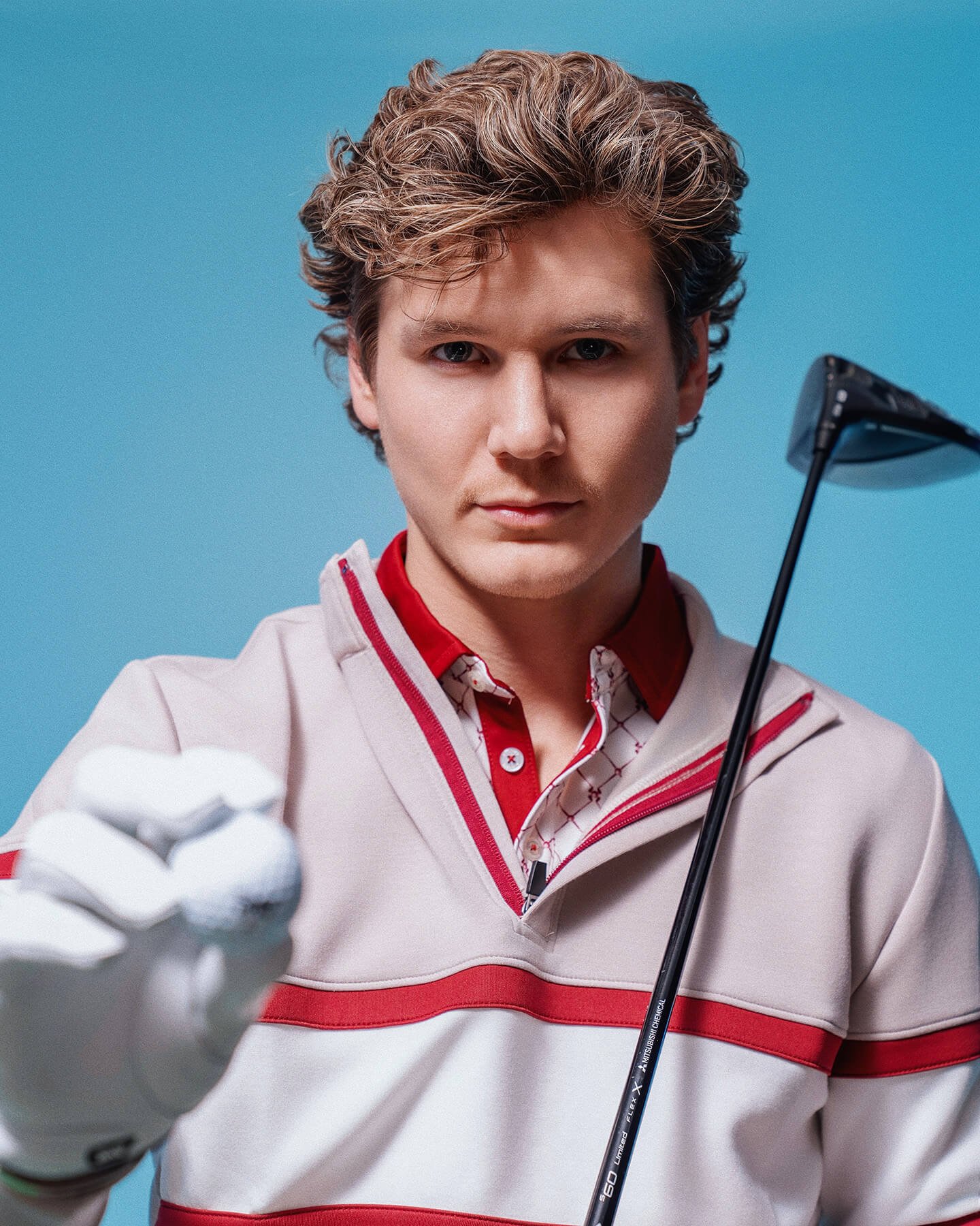 Portrait of a male model in golf apparel holding a club and pointing toward the camera, styled for a commercial golf and sportswear campaign