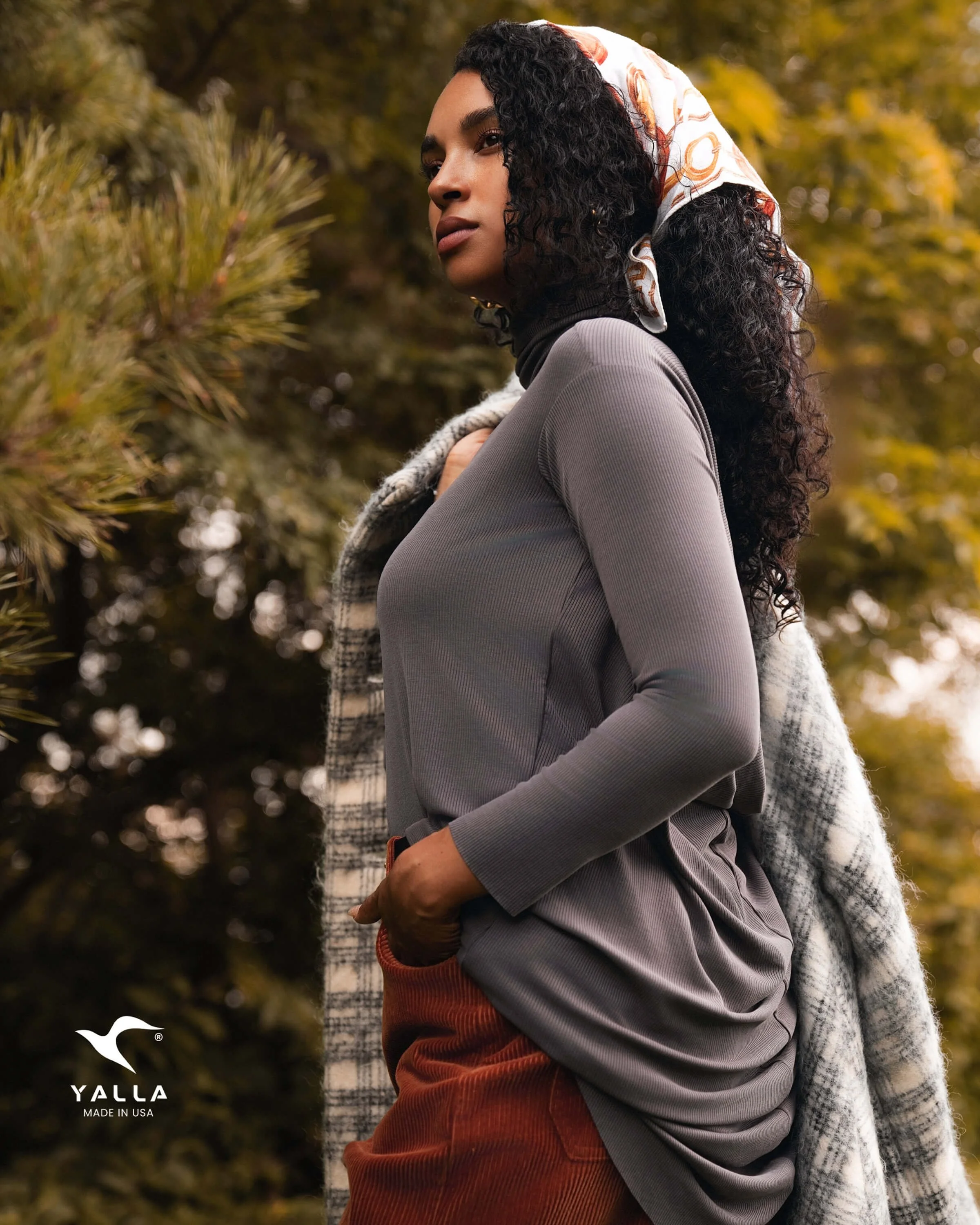 Outdoor portrait of a woman in a headscarf and plaid coat standing among autumn trees, photographed for lifestyle and branding content