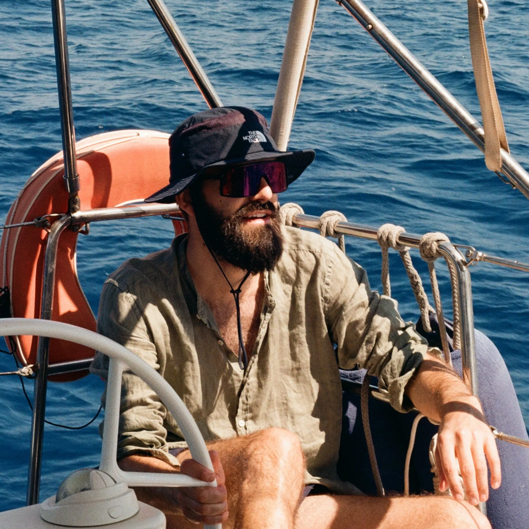Ein Mann mit Bart, Sonnenbrille und Hut sitzt auf einem Boot auf dem Meer.
