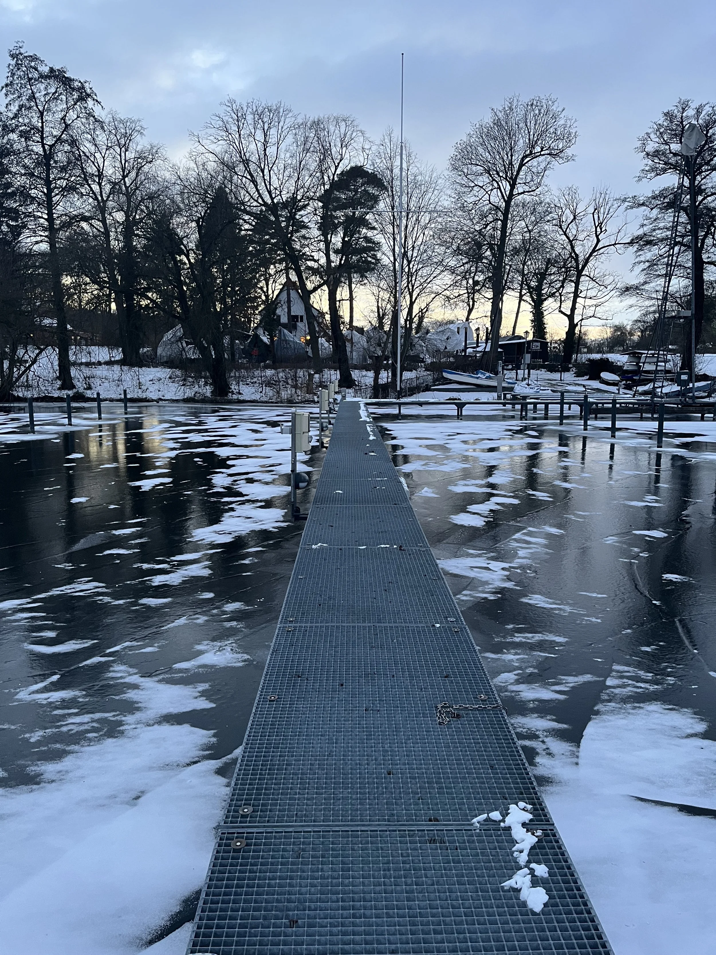 Eisiger Anlegesteg am Fluss mit Gefrorenem Wasser und Bäumen im Hintergrund bei winterlicher Landschaft.