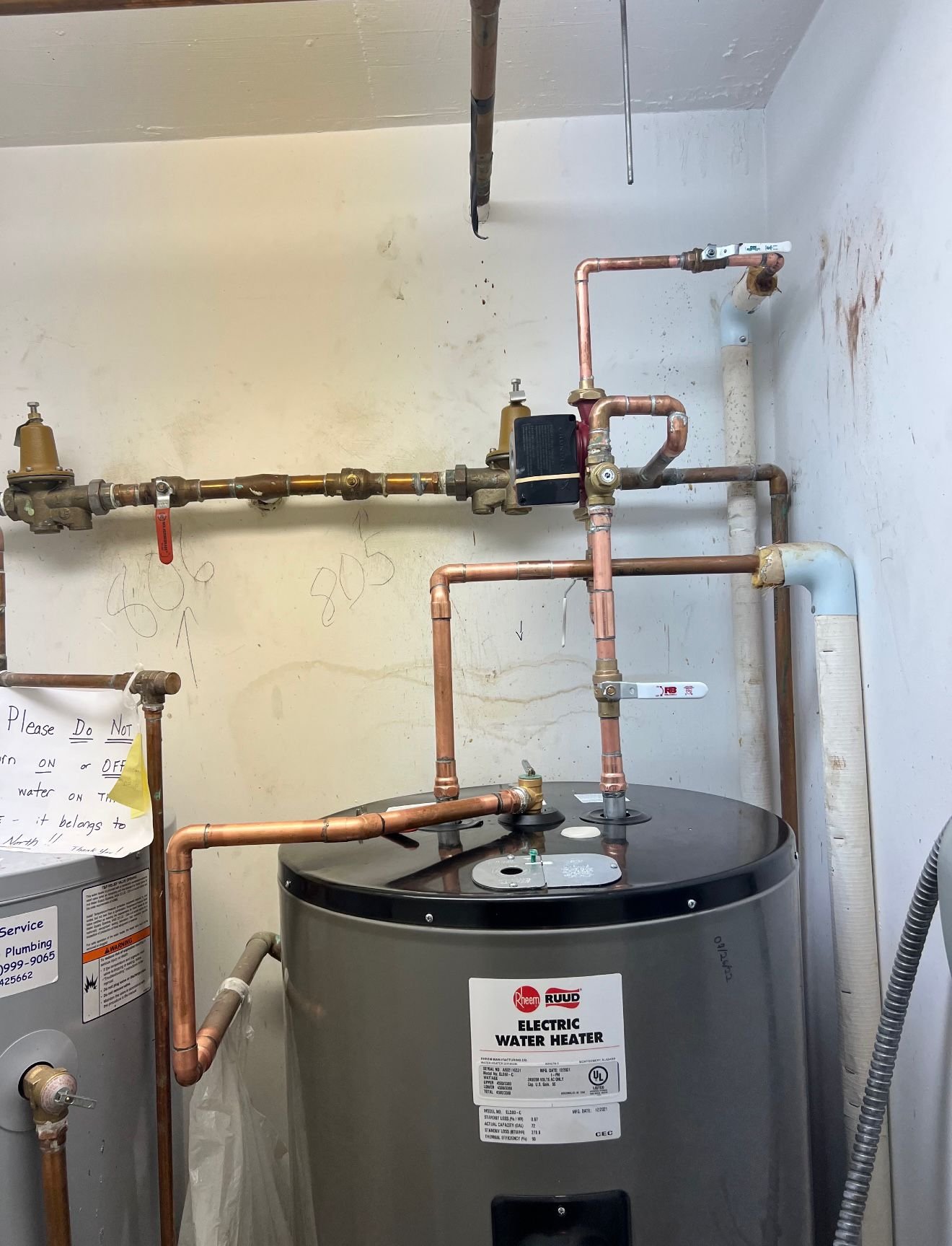 An electric water heater with copper piping connected to it in a utility room.