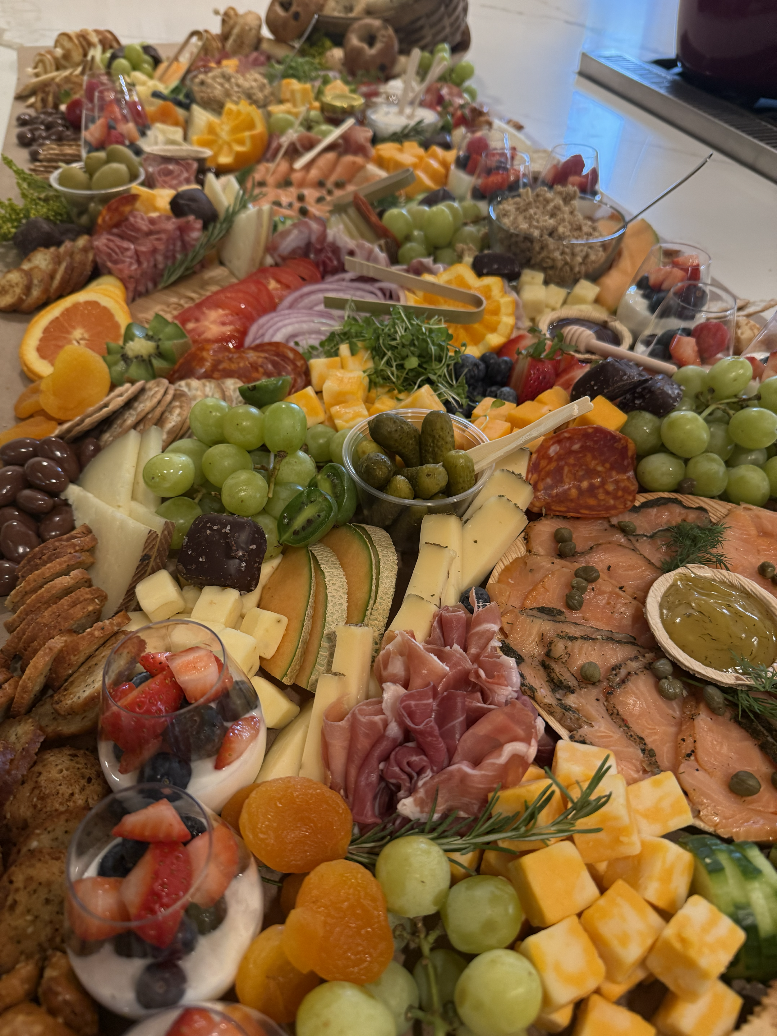 A large charcuterie board filled with assorted cheeses, meats, fruits, crackers, and garnishes.