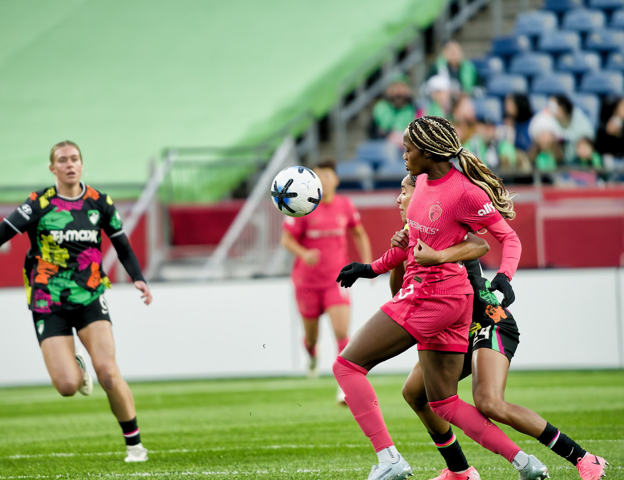 Women playing soccer on a field, with one heading the ball and others running nearby.