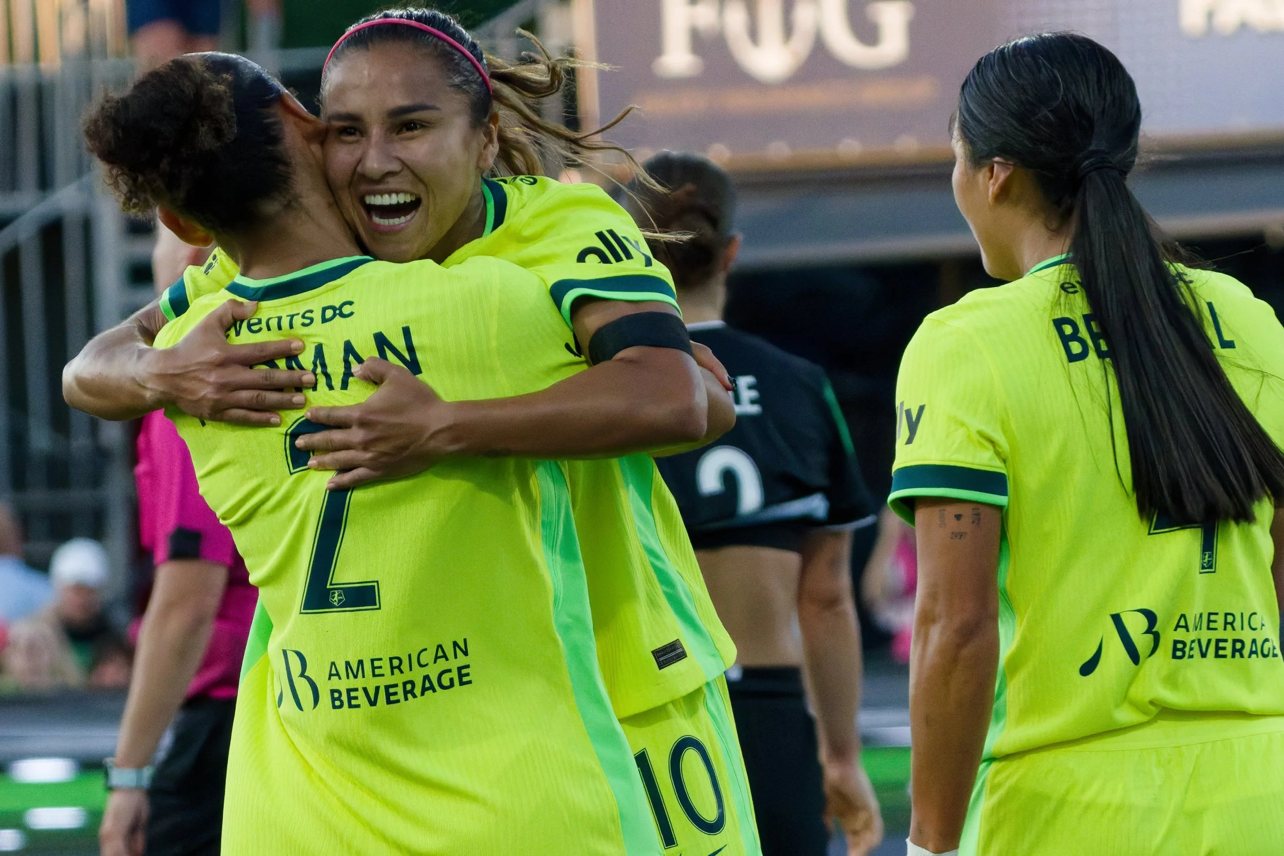 Women in yellow jerseys celebrating on a soccer field, hugging and smiling.