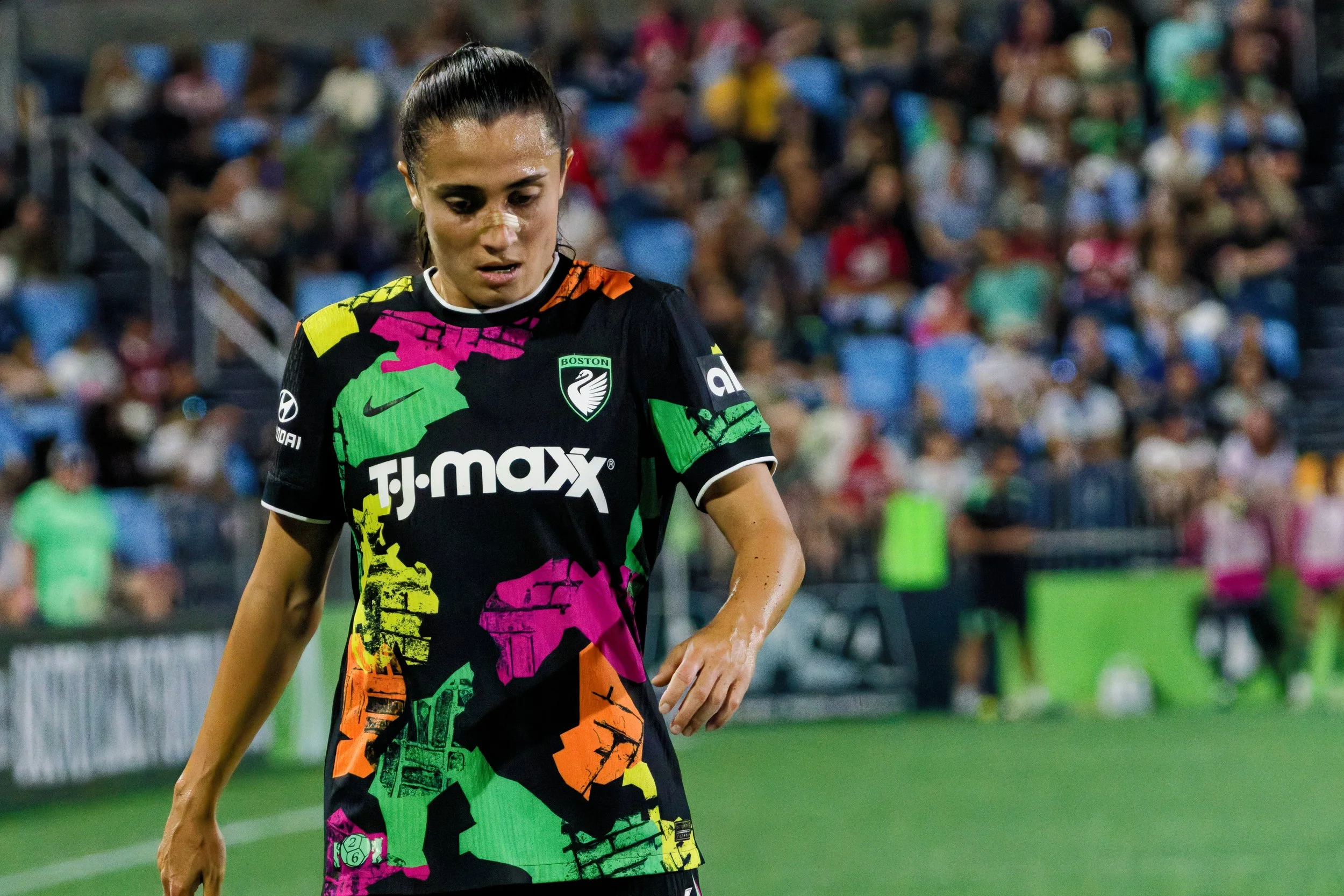 Female soccer player in a colorful uniform on the field with a crowd in the background.