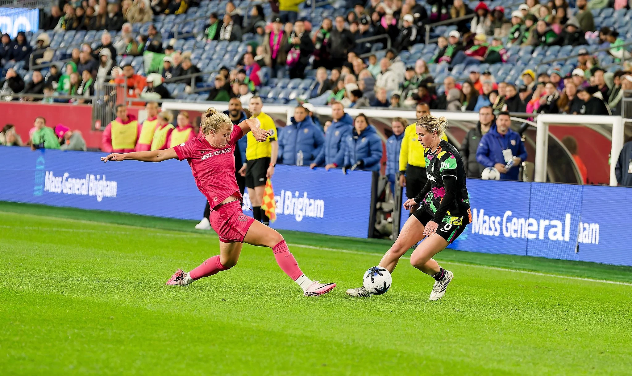 Two soccer players competing for the ball during a match with spectators in the stands.