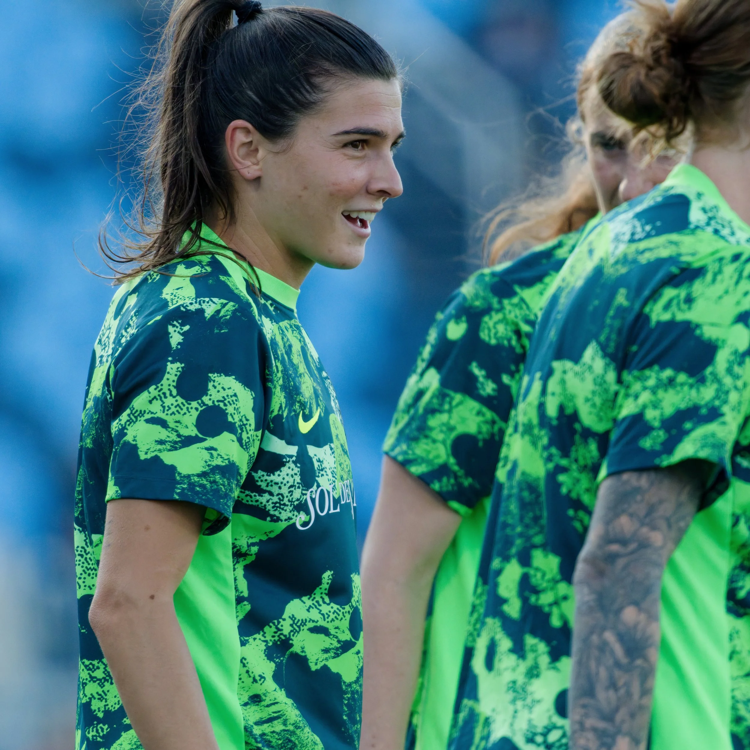 Close-up of young women wearing neon green and black patterned athletic jerseys standing side by side, likely before or after a sports game, outdoors.