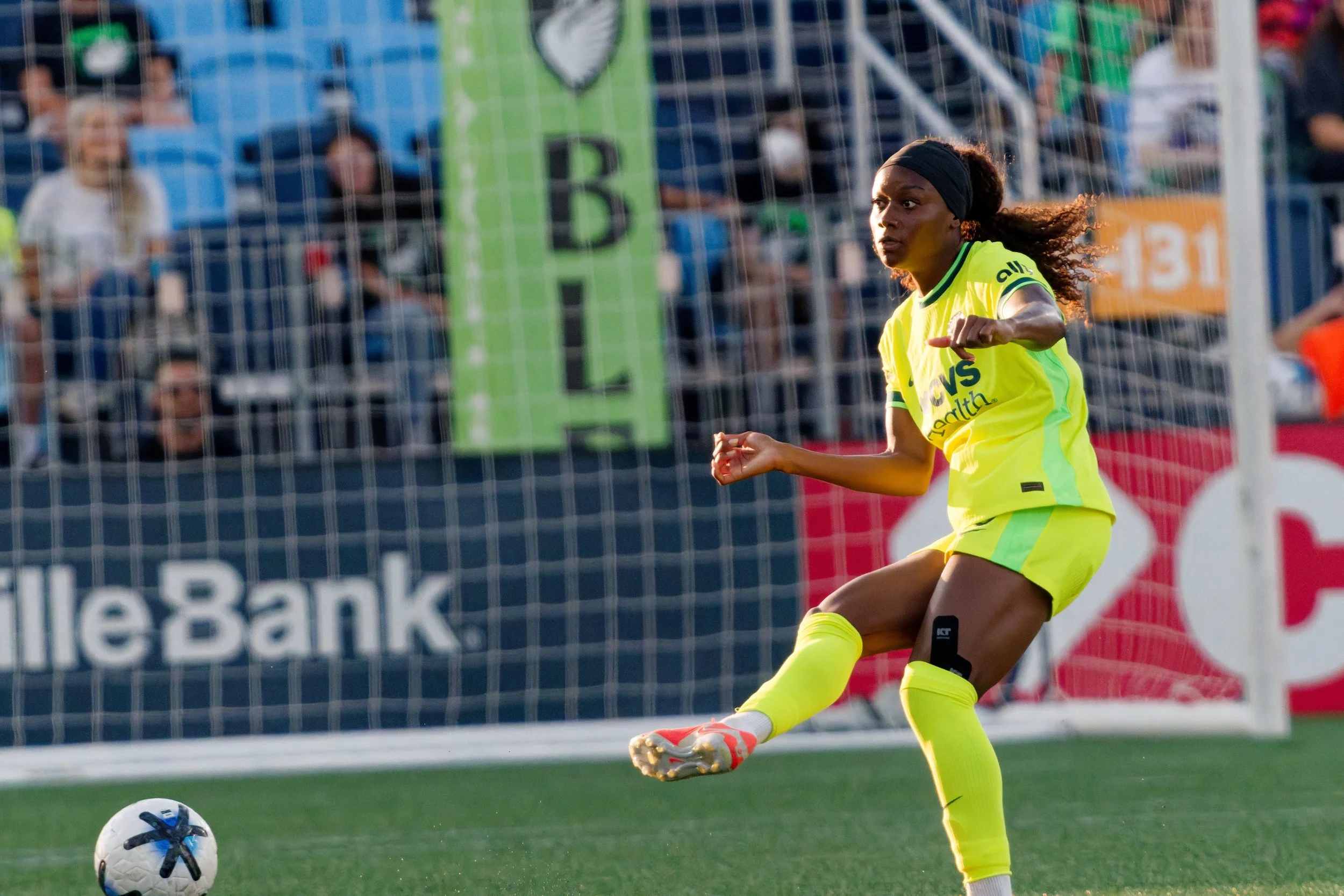 Female soccer player in yellow uniform kicking a soccer ball on the field during a match.