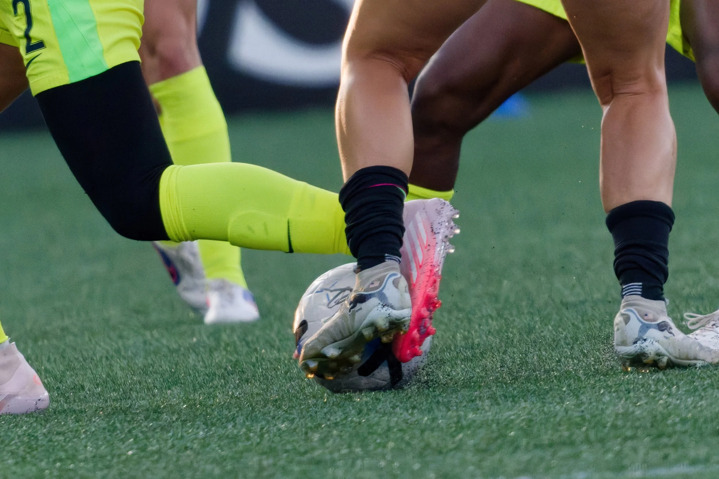 Close-up of soccer players' legs and feet as they scramble for the ball on a grassy field during a match.