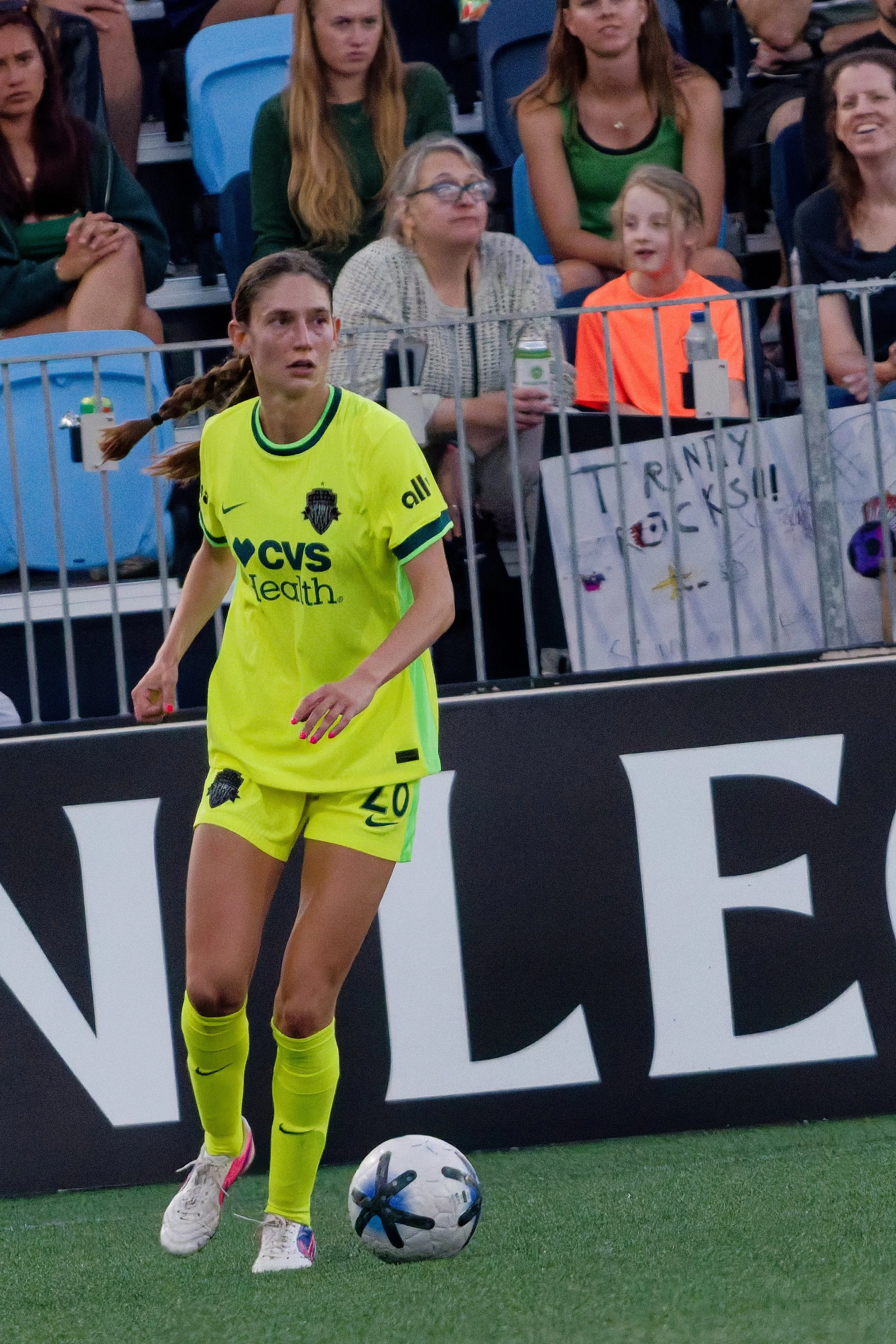 A female soccer player in a bright yellow uniform on a soccer field, with a soccer ball at her feet, preparing for play during a match or practice.
