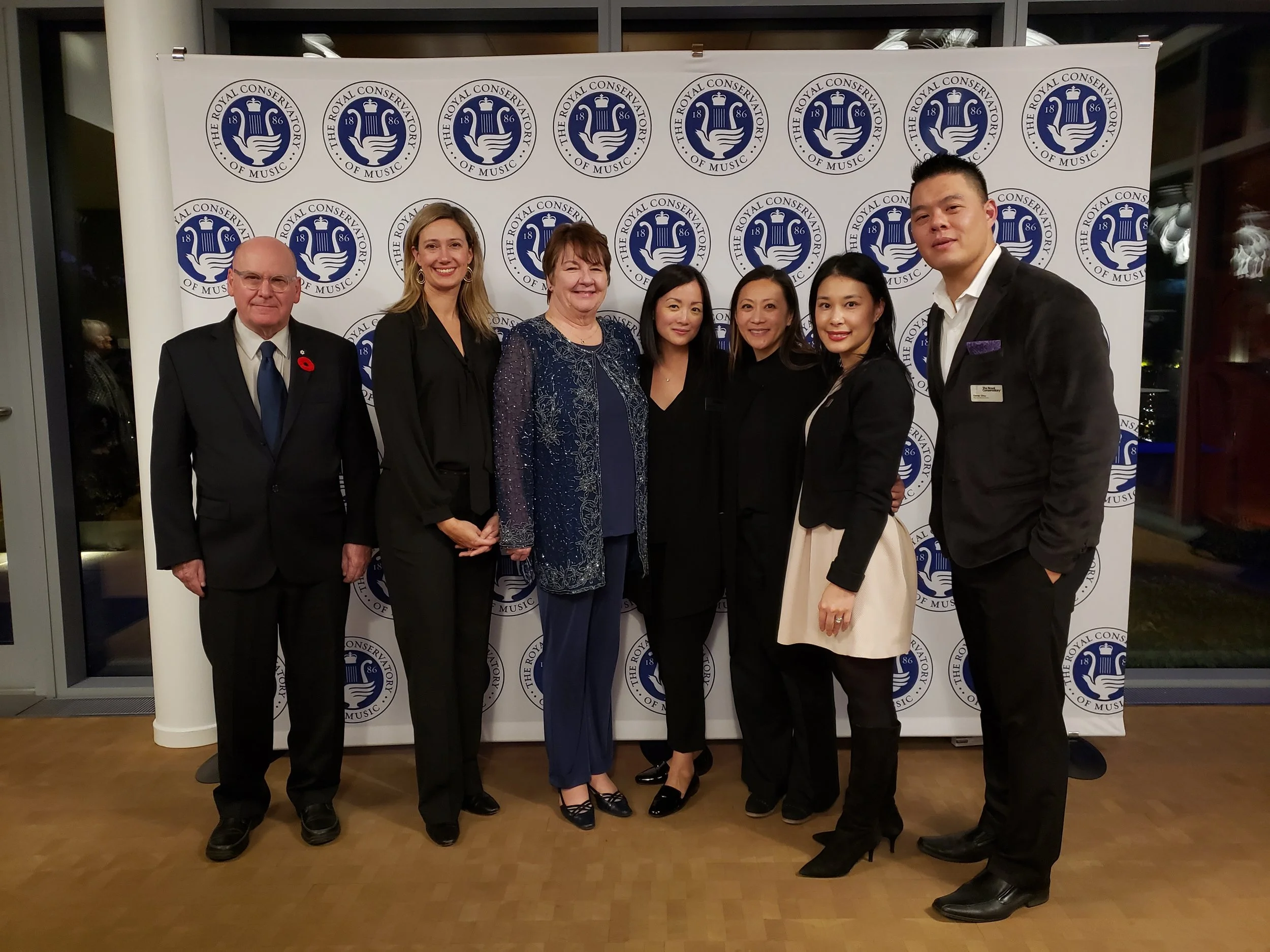Group of seven people standing in front of a backdrop with a logo of The Royal Conservatory of Music, posing for a photo at an event.