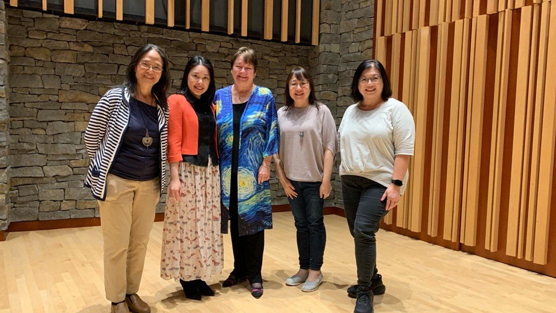 Five women standing together inside a room with stone and wooden walls, smiling for the photo.