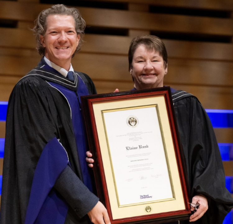 A man and a woman in academic regalia standing together, holding a framed certificate during a graduation ceremony.