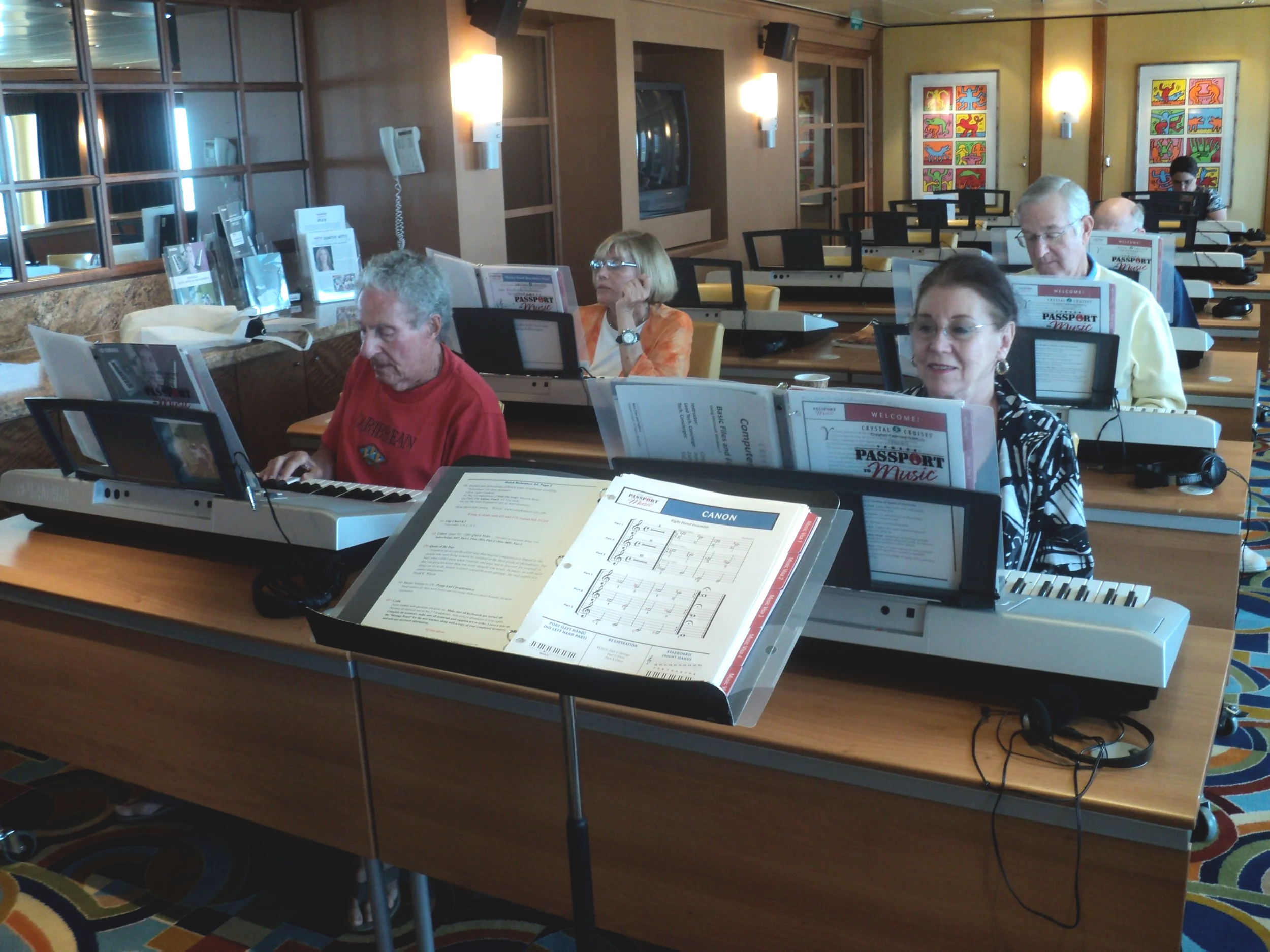 Group of people playing electronic keyboards at a music class or workshop in a spacious room with colorful artwork on the walls.
