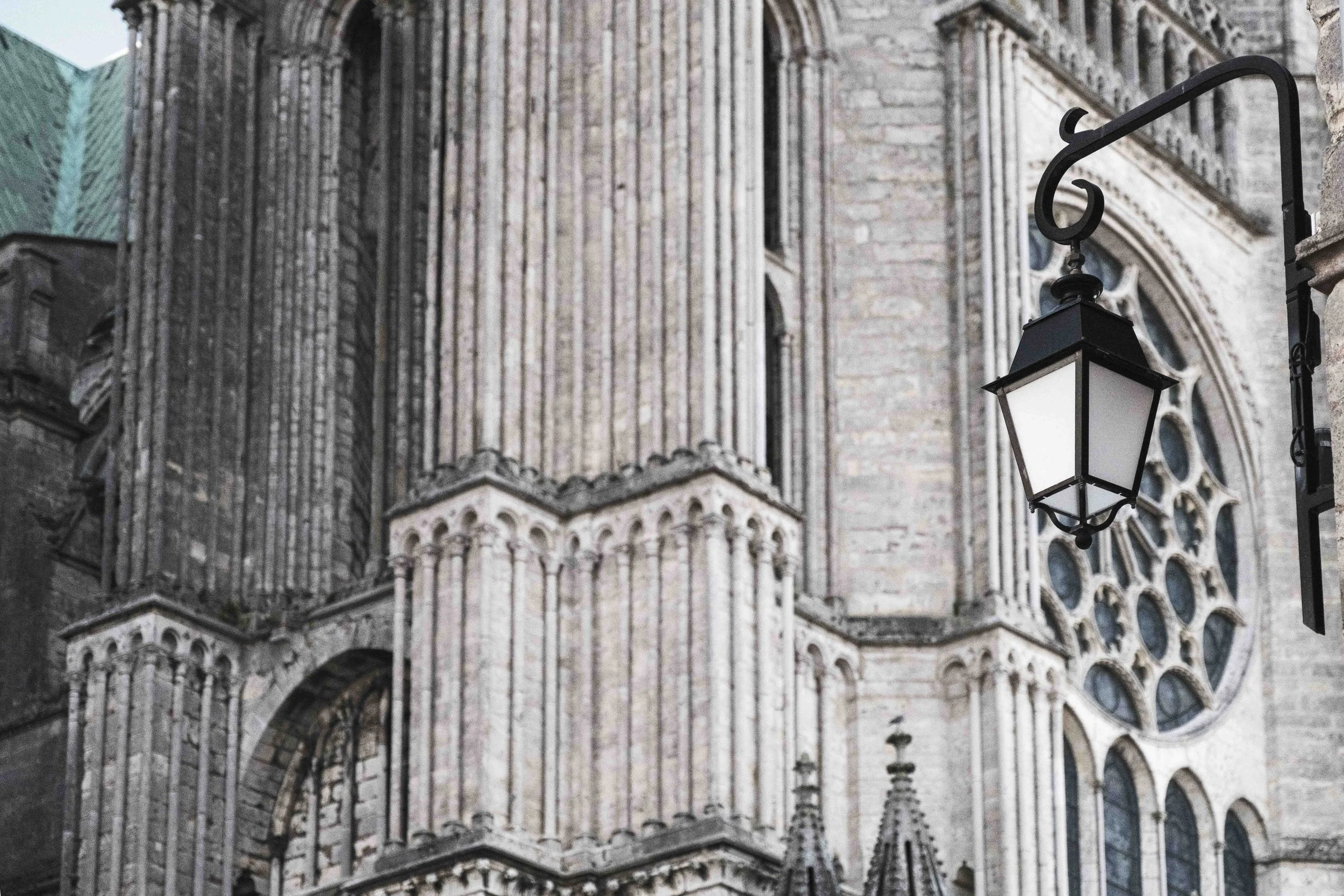 Ein gotisches Kirchengebäude mit hohen, ornamentalen Fenstern und steinernen Fassaden. Im Vordergrund ist eine schwarze Laterne an einem Laternenmast zu sehen.