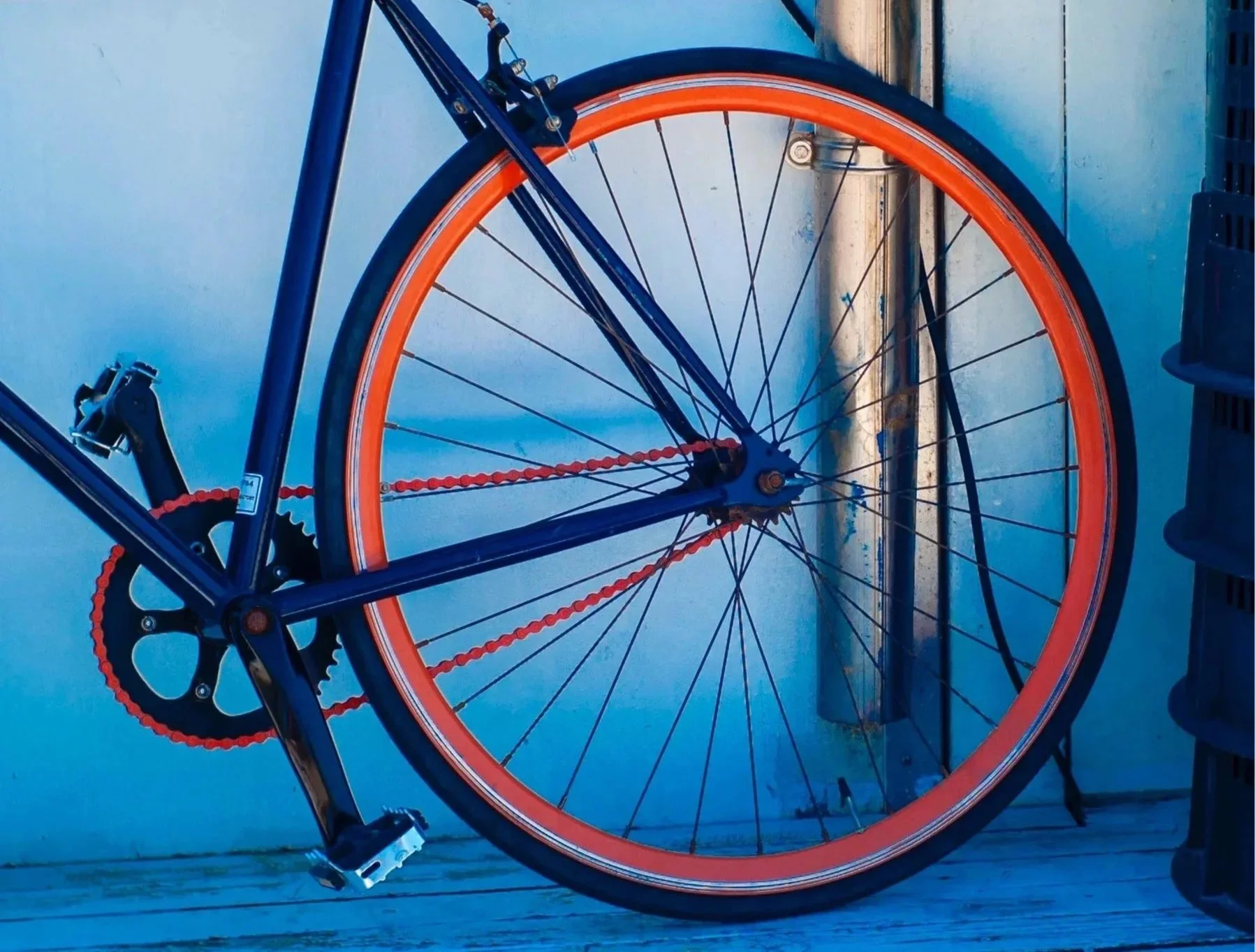Ein Fahrrad mit blauer Rahmen und orange Reifen steht an einer Wand, die durch eine vertikale Stange durchquert wird.