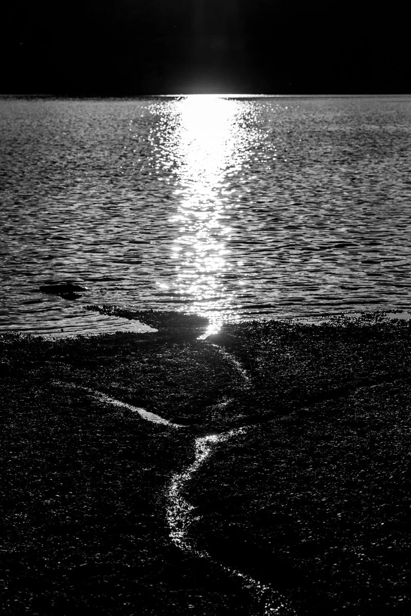 Sonnenuntergang spiegelt sich auf dem Wasser, Blick von einem Kiesstrand