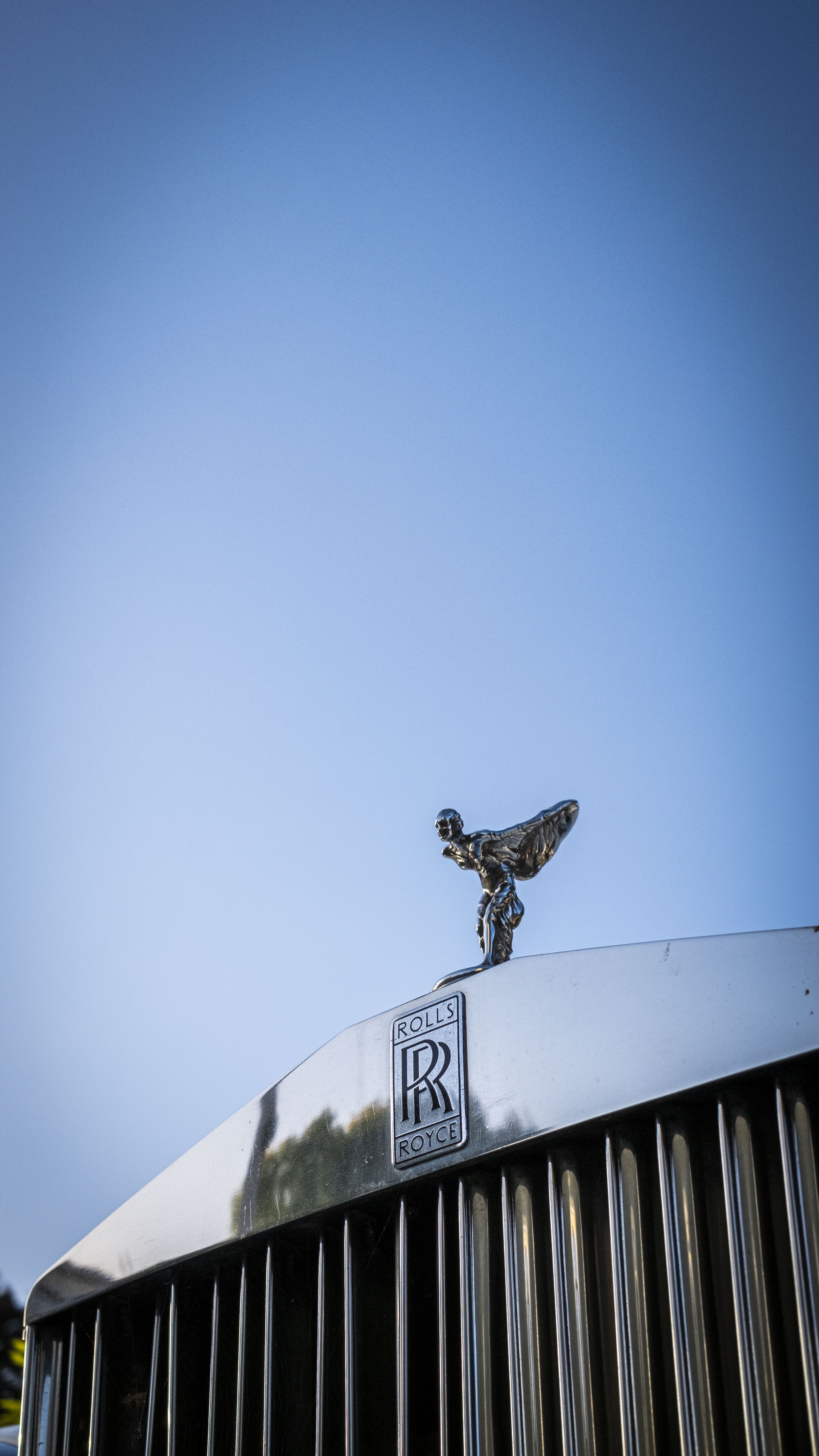 Ein silberner Rolls-Royce Auto mit der ikonischen Spirit of Ecstasy Figur auf der Motorhaube, aufgenommen bei Sonnenuntergang oder an einem klaren Tag.