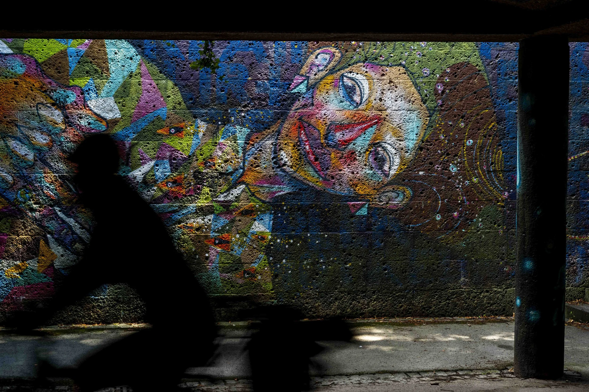 Ein farbenfrohes Graffiti an einer Betonwand in einem Tunnel mit einem Schatten im Vordergrund.