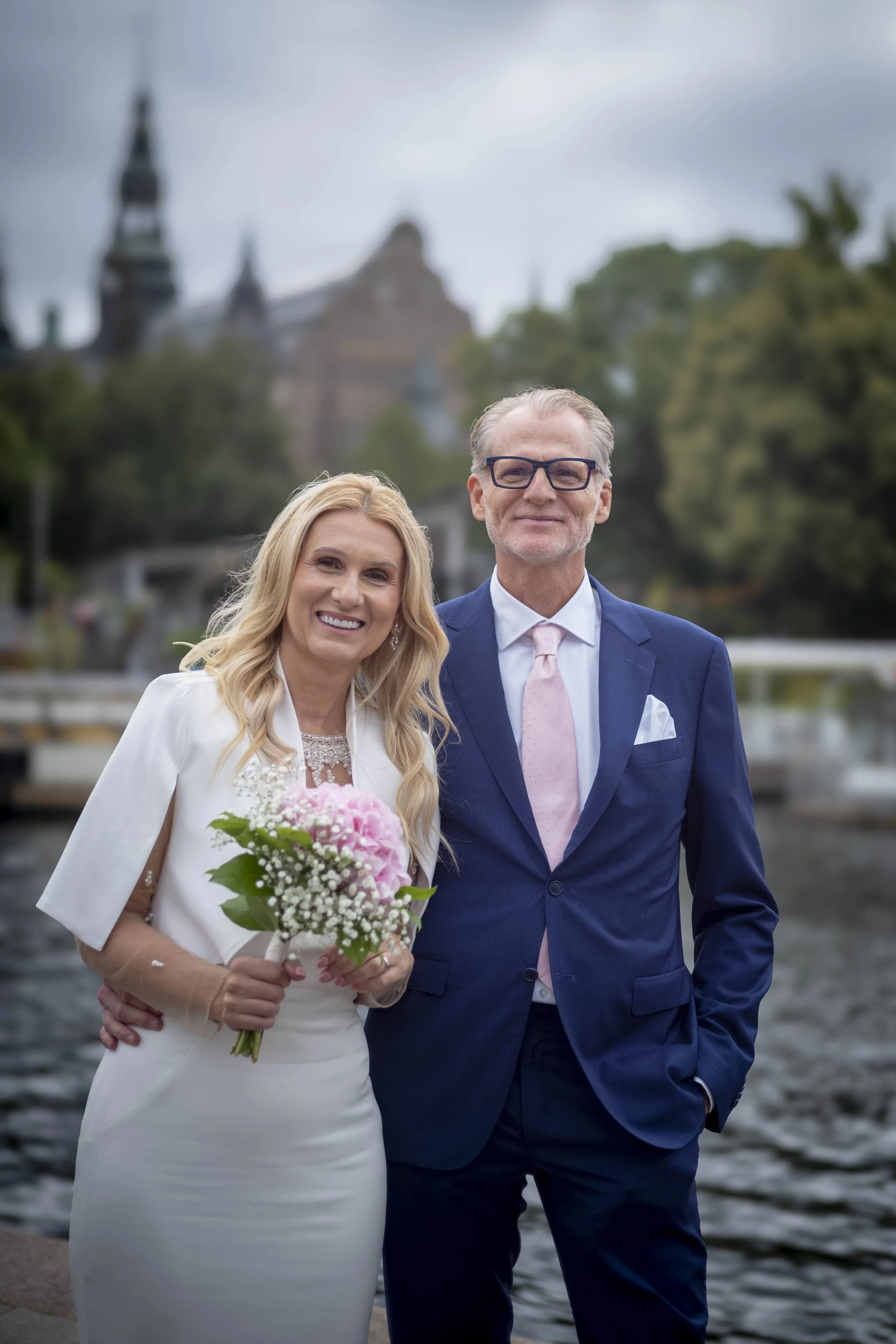 Ein Paar bei einer Hochzeit, die Frau hält einen Blumenstrauß, der Mann trägt einen blauen Anzug mit einem pinken Krawatte.
