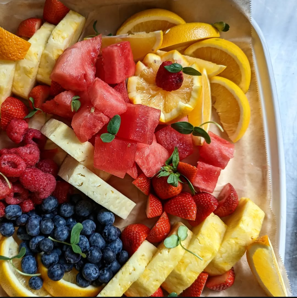 Assorted fresh fruit slices including strawberries, blueberries, raspberries, watermelon, pineapple, and lemon arranged on a tray.