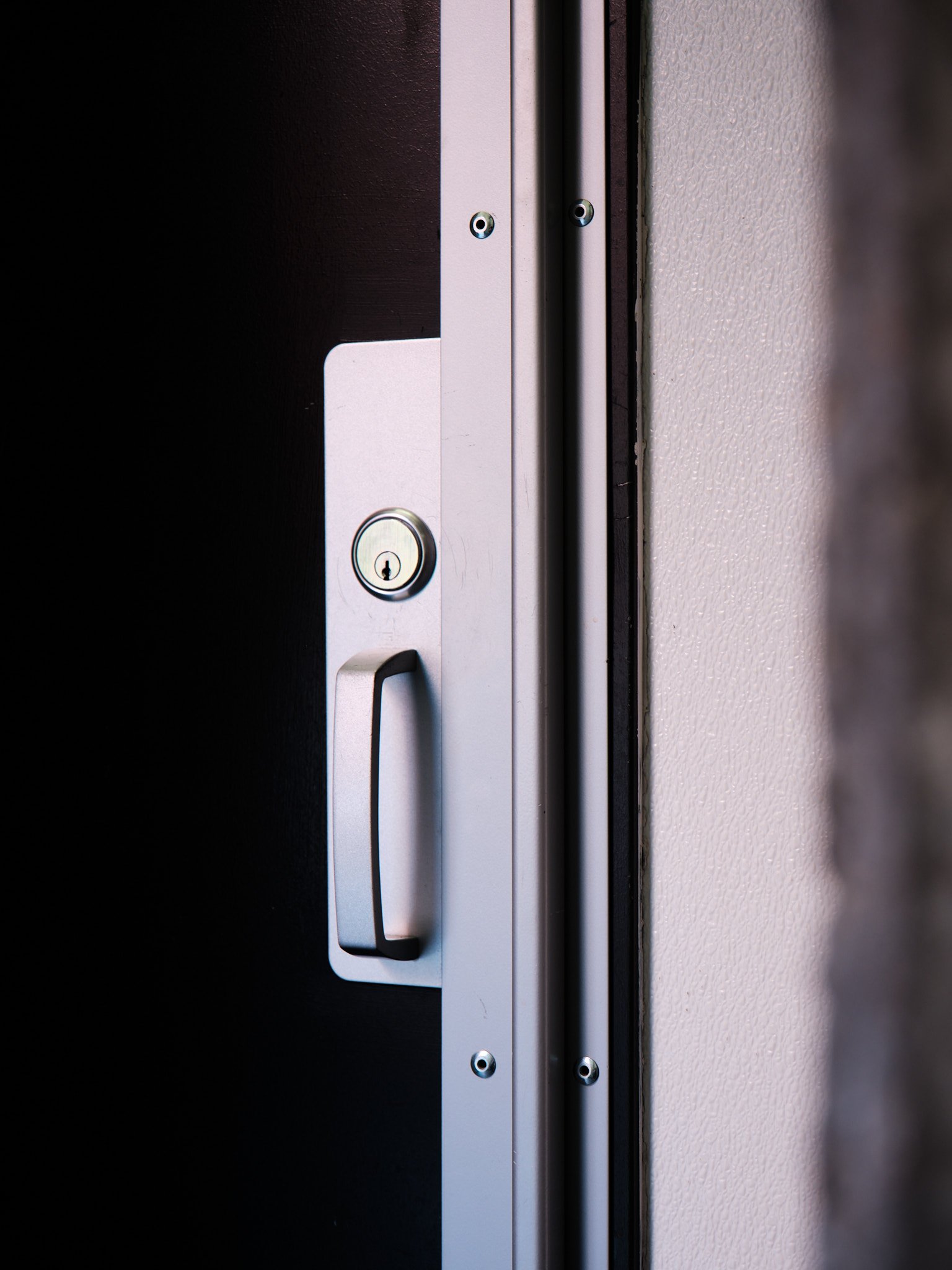 Close-up of a door lock and handle on a white door with a beige wall on the right side.