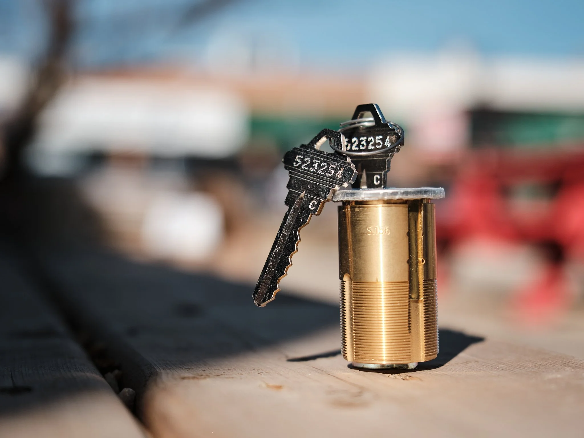 Close-up of a brass lock with keys hanging from it, set against a blurred background under a cloudy sky.