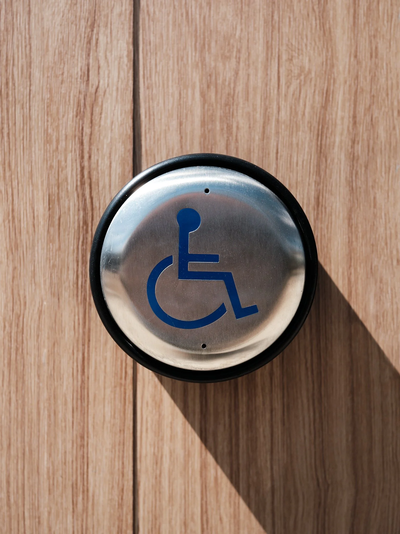 Close-up of a handicap-accessible door button with a wheelchair symbol, mounted on a wooden wall.