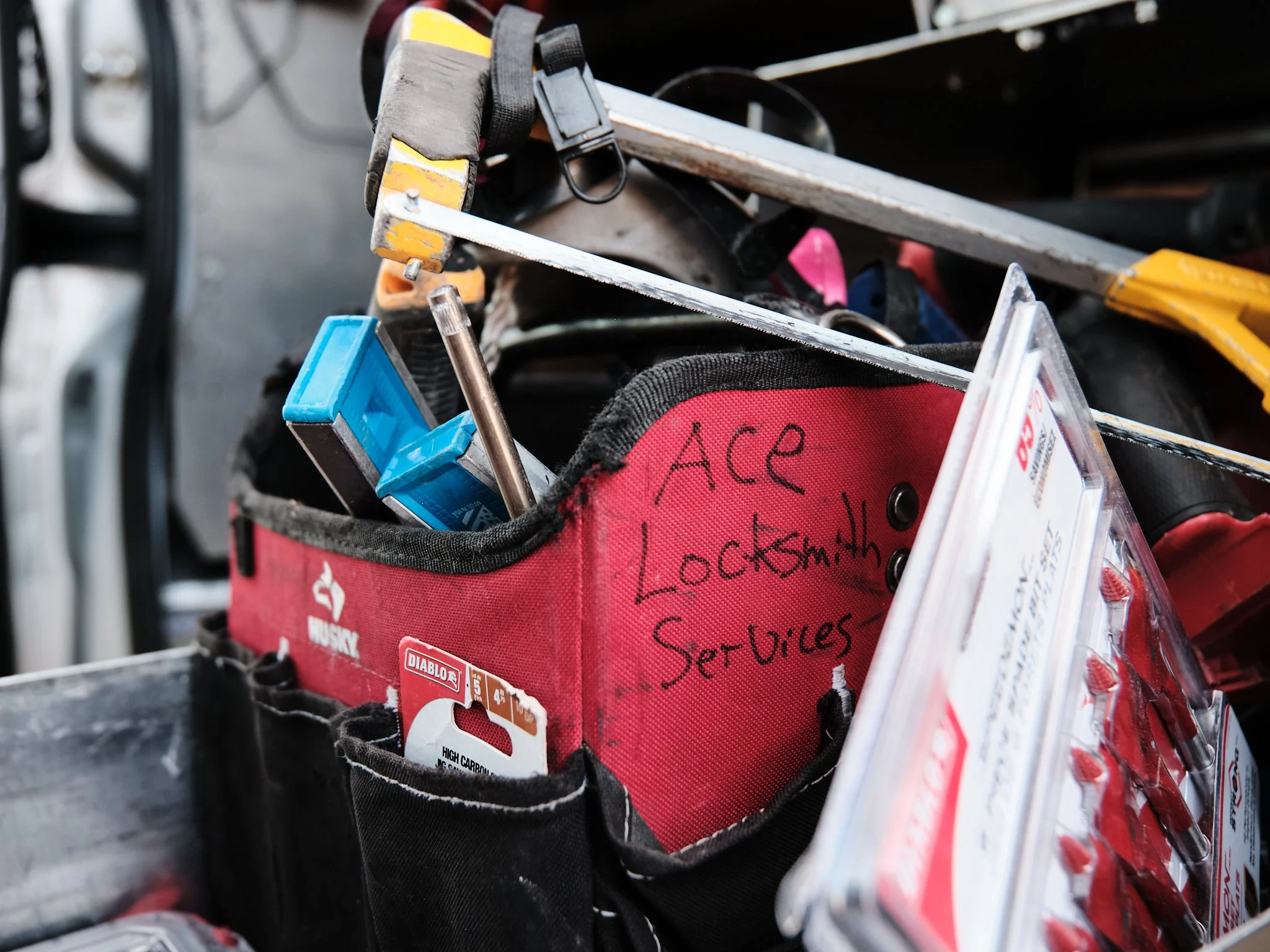 A red toolbox with handwritten text on the side – "Ace Locksmith Services Inc." – which is a locksmith based in Edmonton, Alberta. Various tools and supplies are in the box, including a black and yellow screwdriver, and a metal ruler.