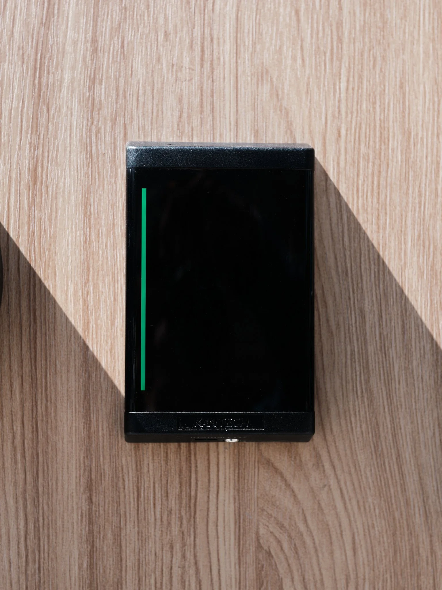 A black electronic device with a green vertical line on the left side, placed on a wooden surface, with the brand name 'Kantech' visible at the bottom.