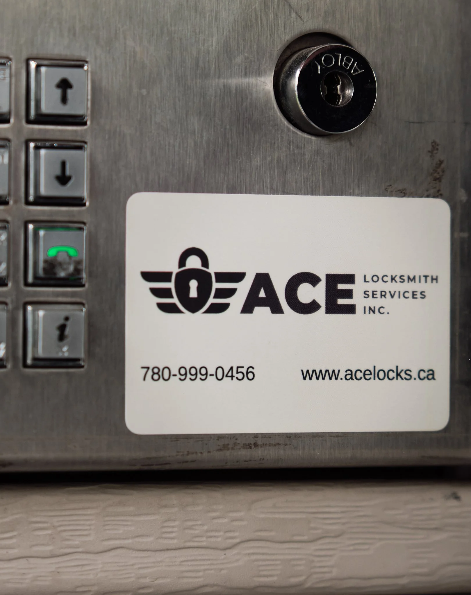 Close-up of a building intercom with an "Ace Locksmith Services" sticker on it, that includes a phone number and website.