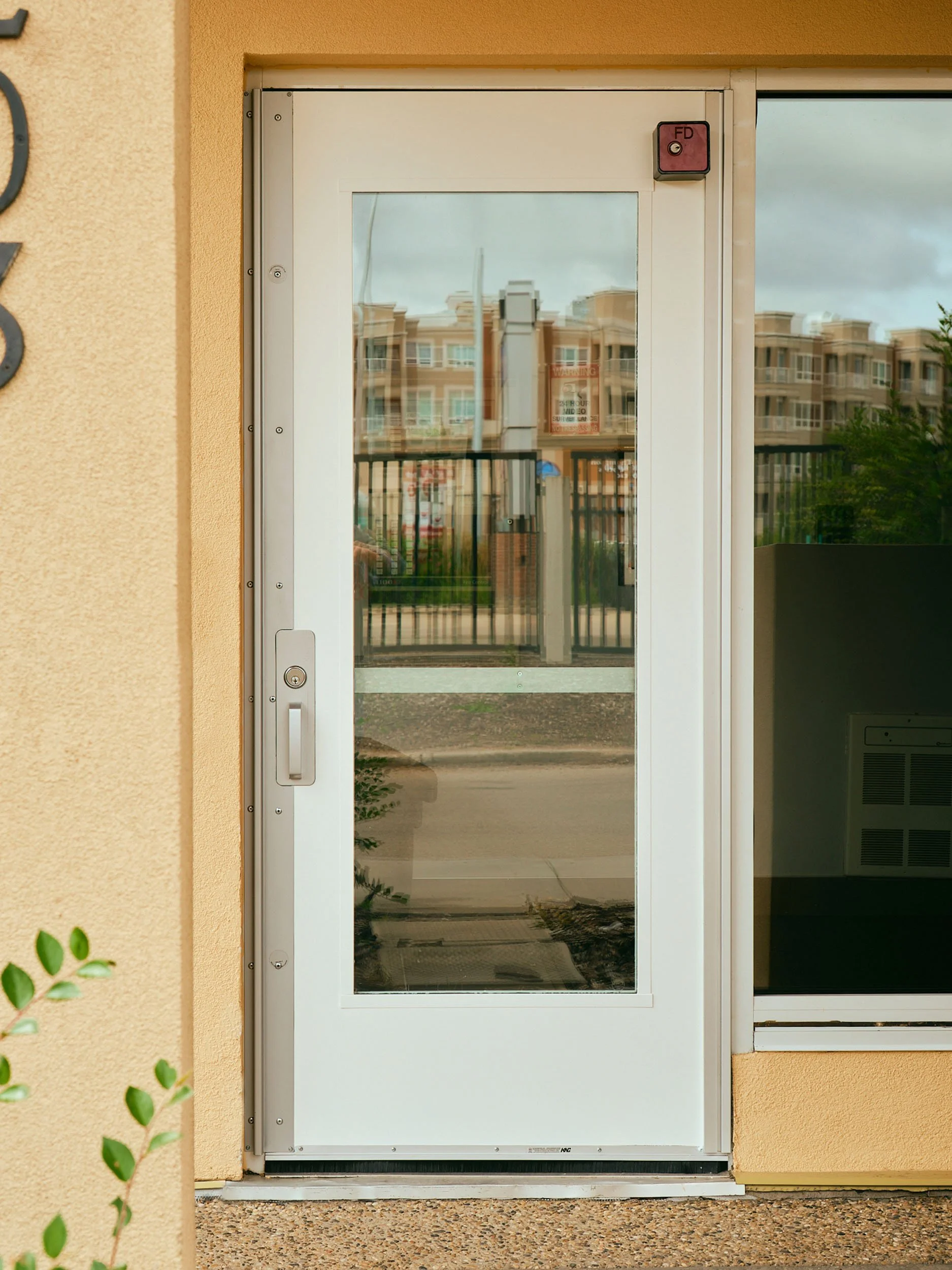 A glass door with a metal frame on a building exterior, reflecting nearby residential buildings and a cloudy sky.