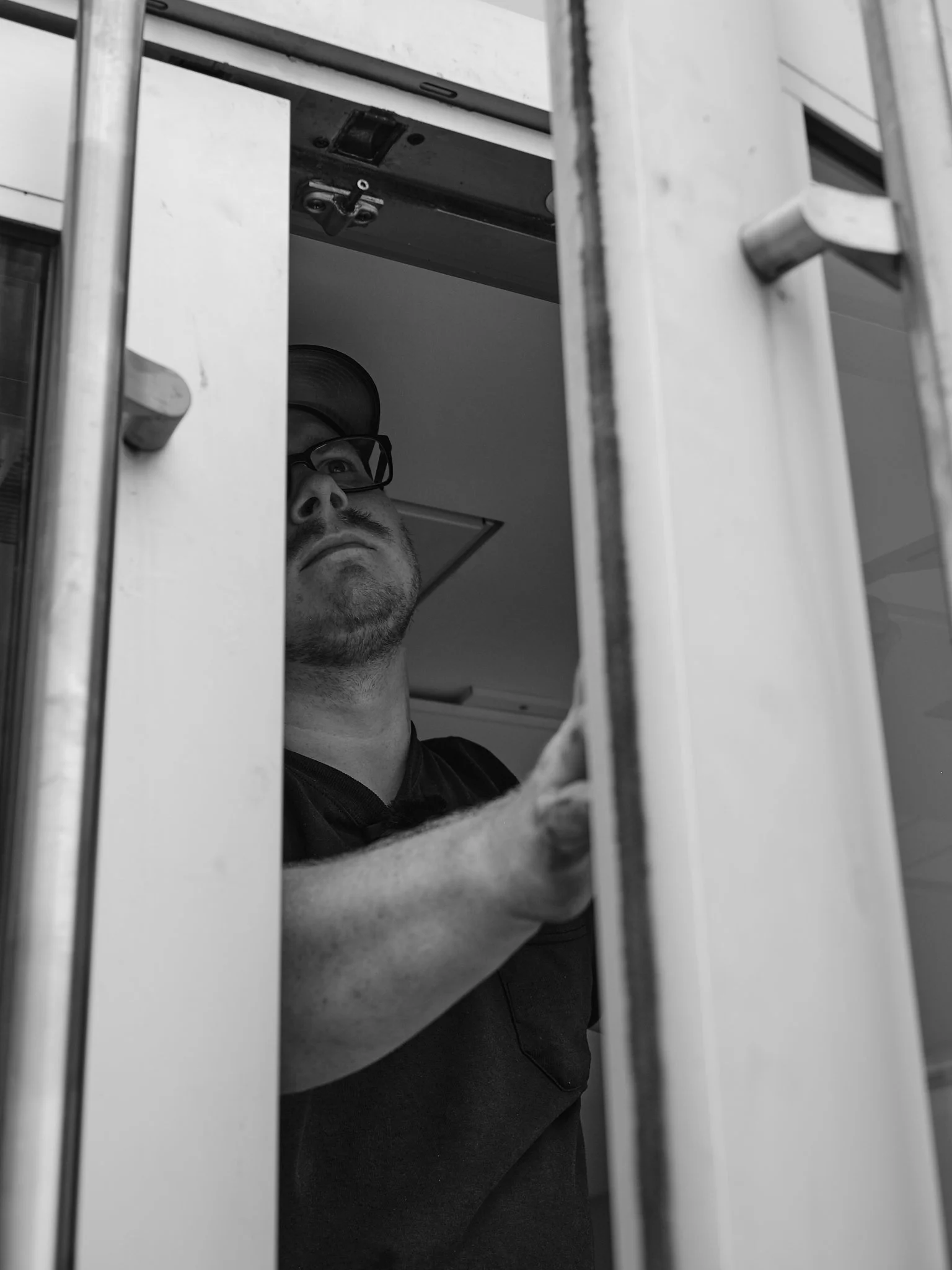 A locksmith with glasses and a hat working on a commercial door at a rec centre.