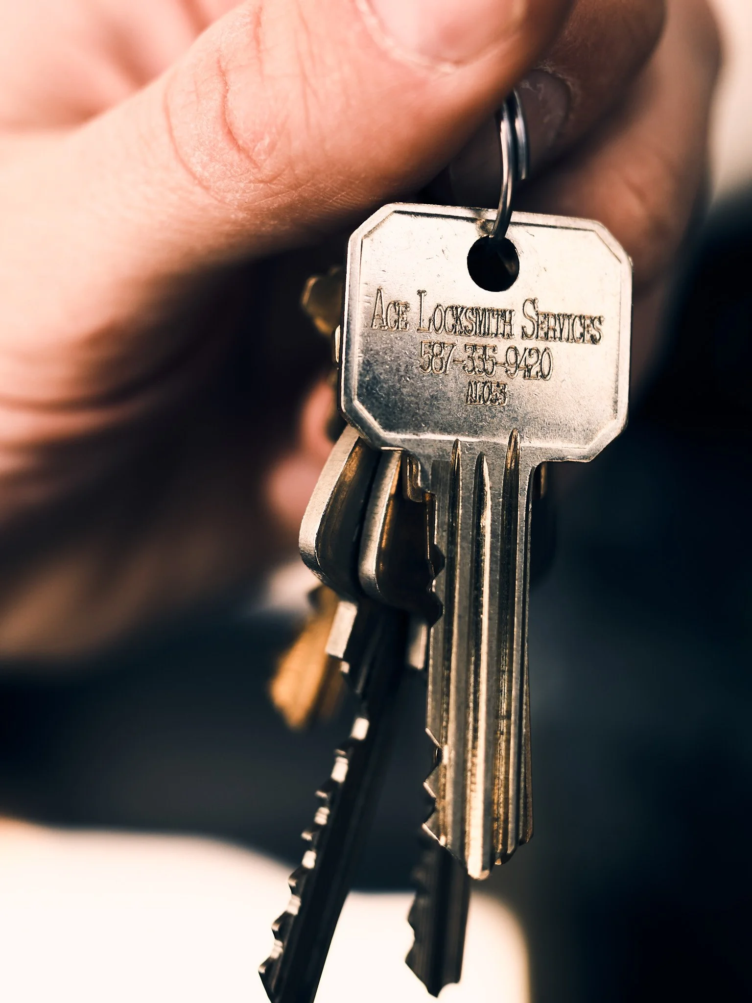 Close-up of a metal key held with fingers, engraved with the words 'Ace Locksmith Services' and a phone number.