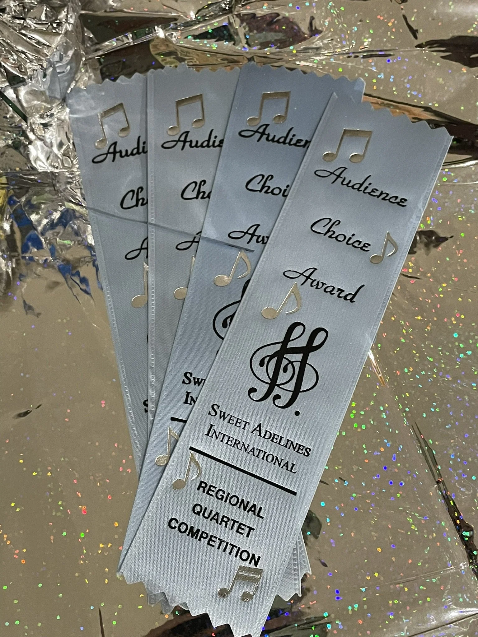 Four bookmarks with ribbons reading 'Audience Choice Award,' featuring musical notes and a stylized 'S.' The bookmarks mention 'Sweet Adelines International,' 'Regional Quartet Competition,' and are set on a glittery, holographic background.