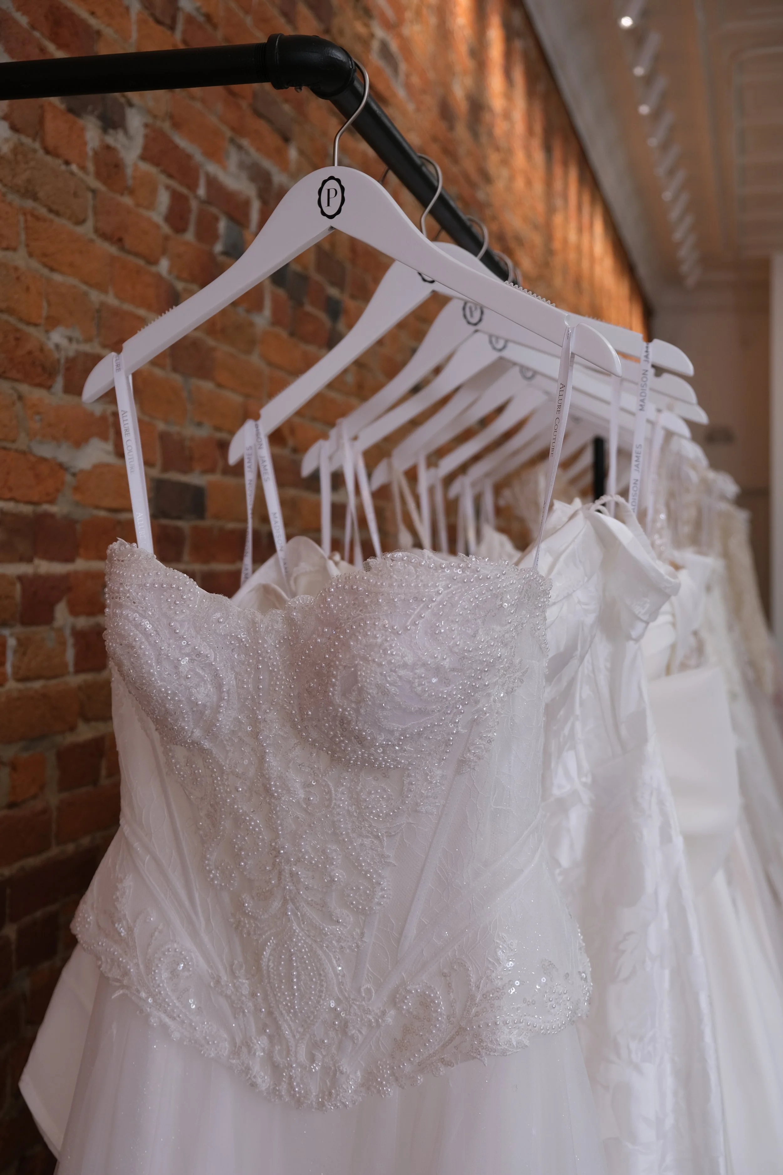 Wedding dresses hanging on white hangers on a black metal rod against a brick wall.