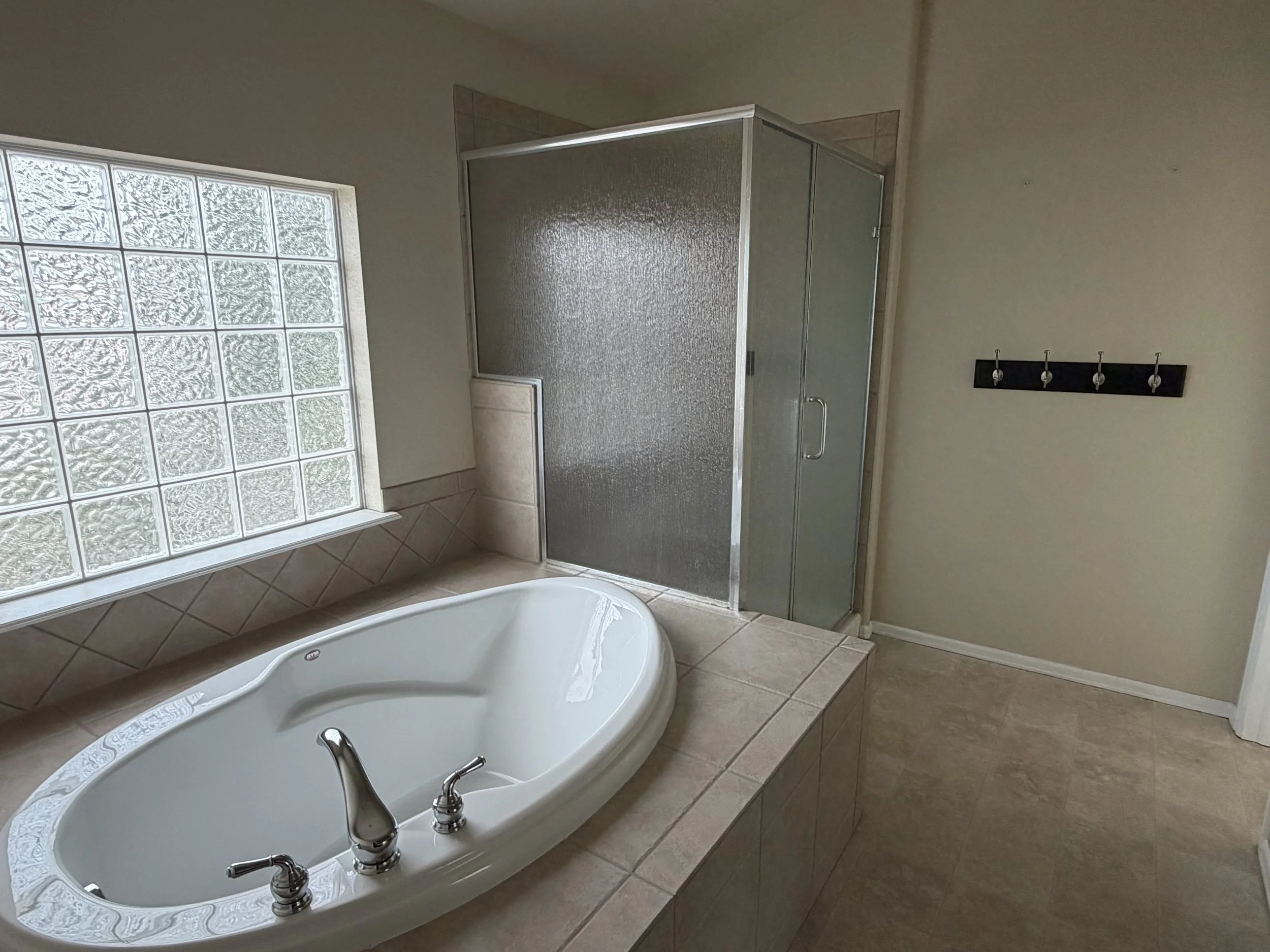 Bathroom with glass block window, bathtub, tiled floor, and shower with frosted glass door.