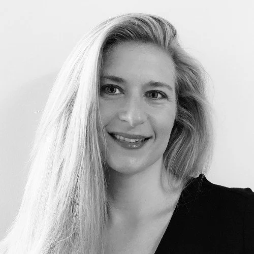 Black and white portrait of a smiling woman with long, wavy hair wearing a dark top.