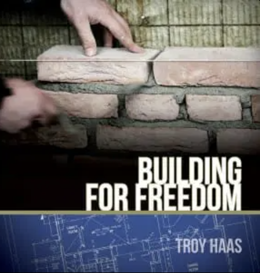 A person building a brick wall with the phrase 'Building for Freedom' overlayed.