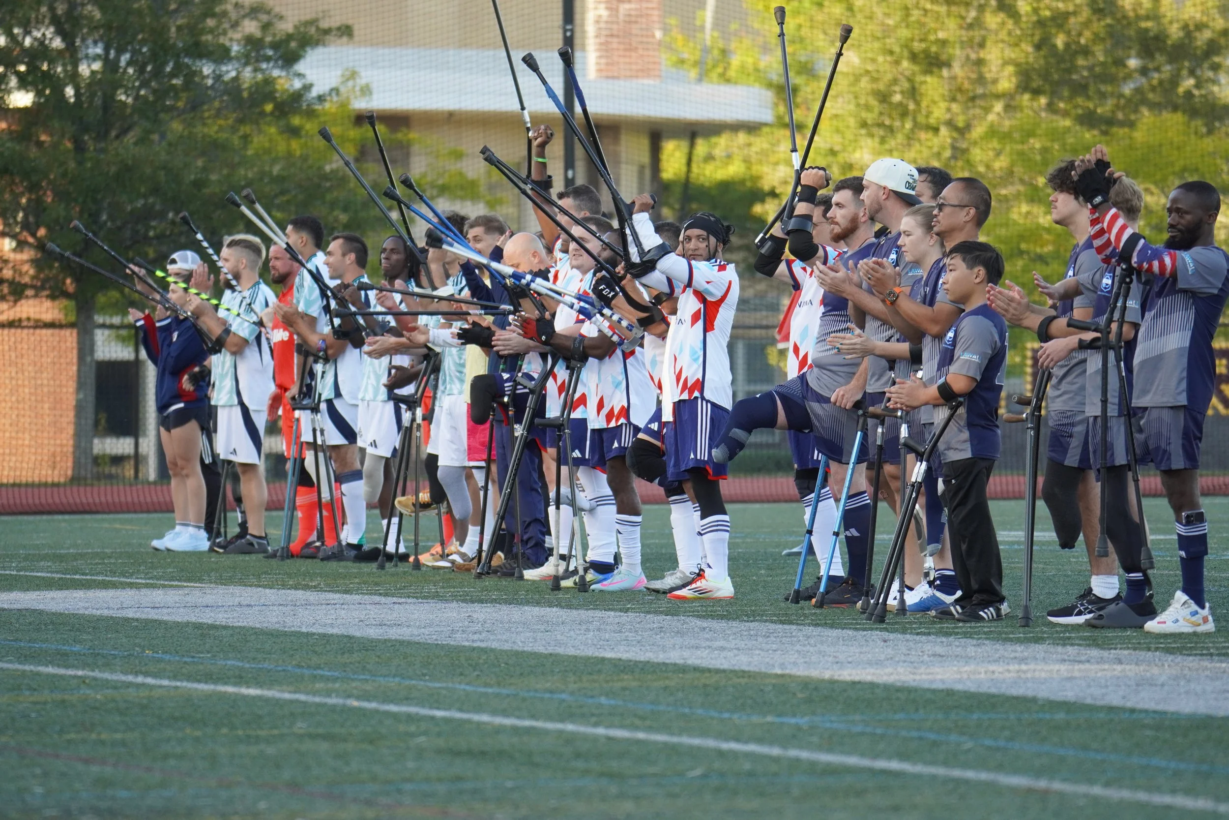 A line of athletes and team members on a sports field, holding up crutches while applause.