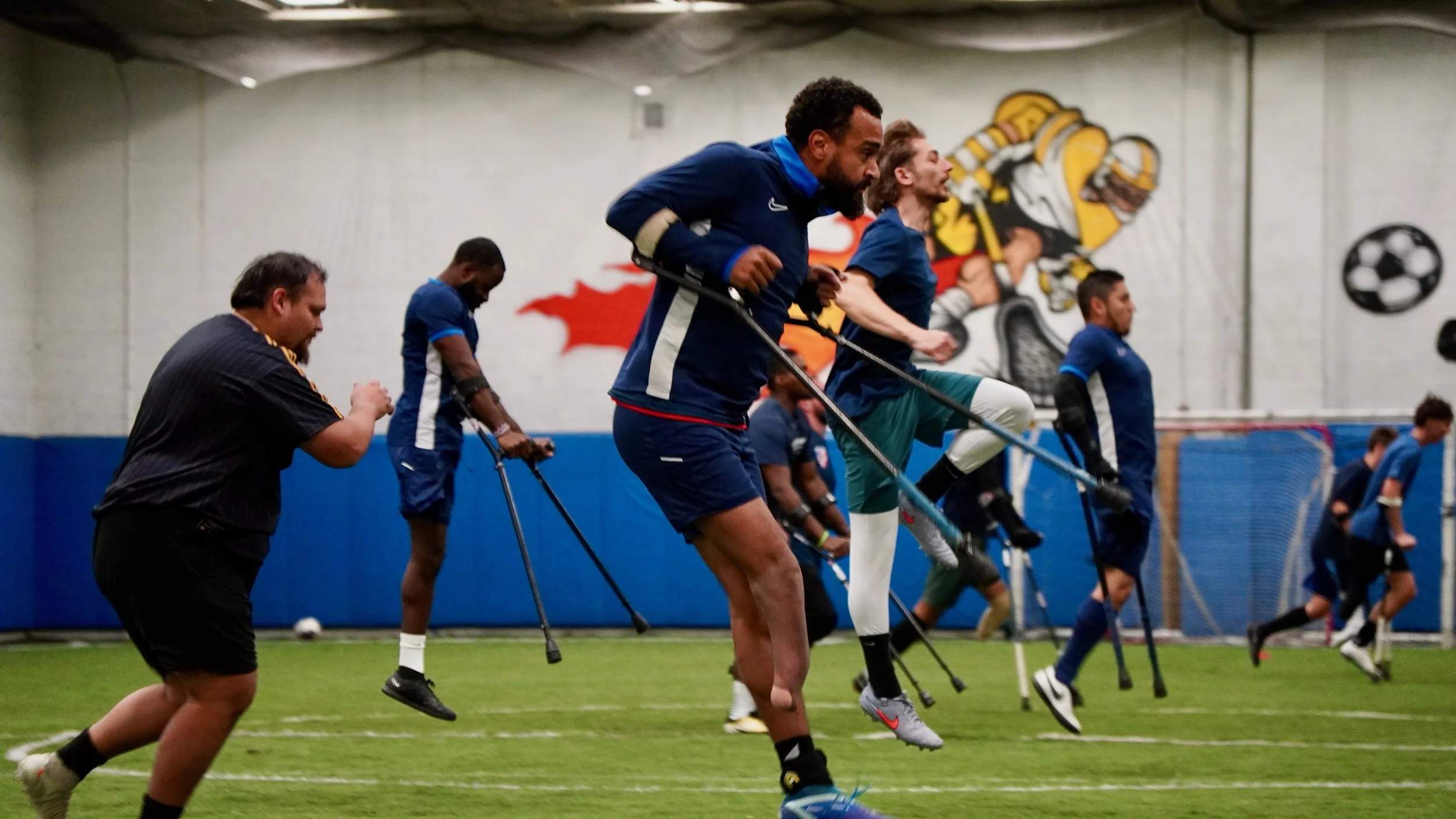 Group of athletes practicing soccer drills indoors, running with resistance bands on a grass field.