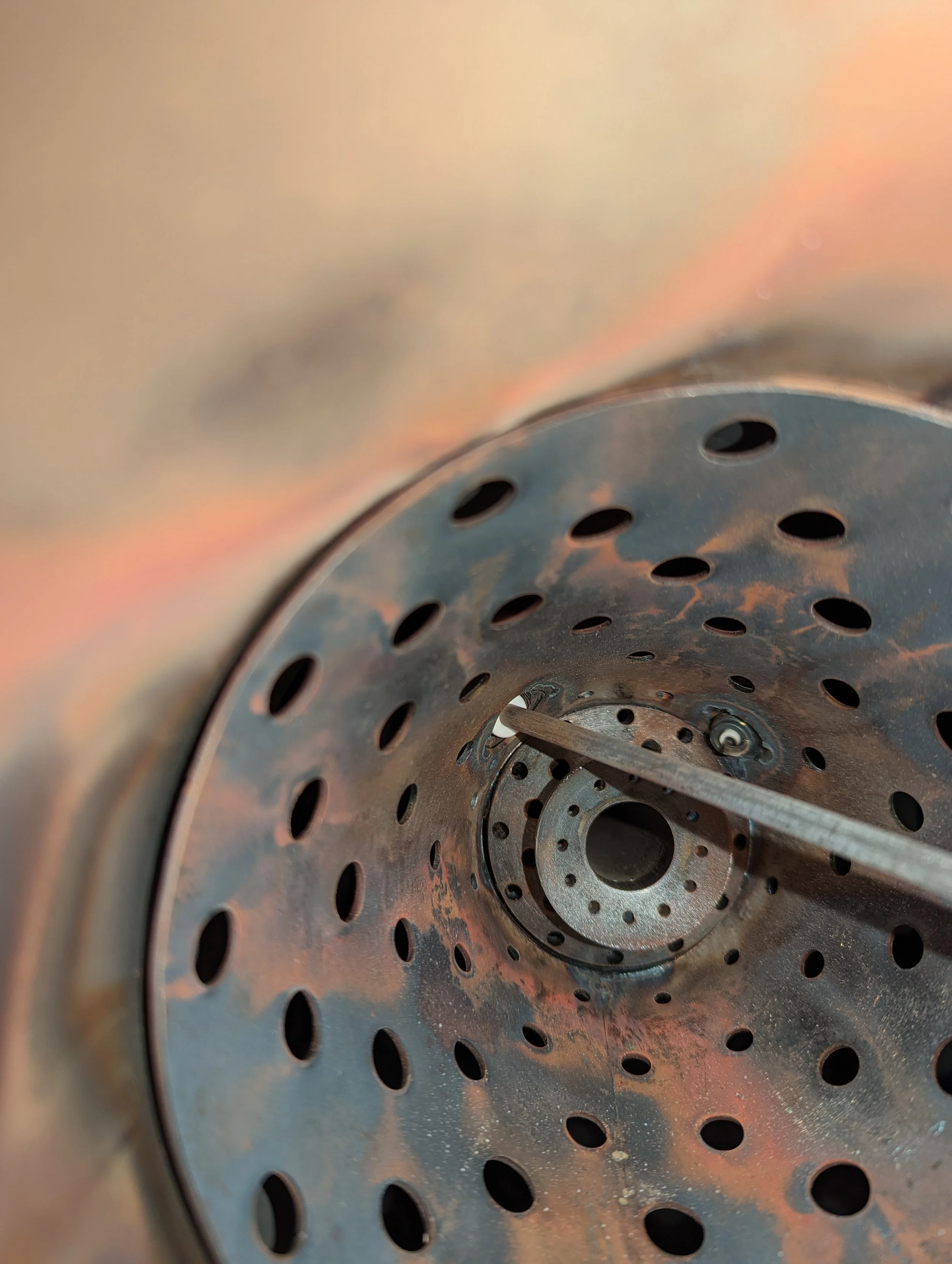 Close-up view of a metallic, perforated surface with holes arranged in concentric circles, showing rust and weathering.