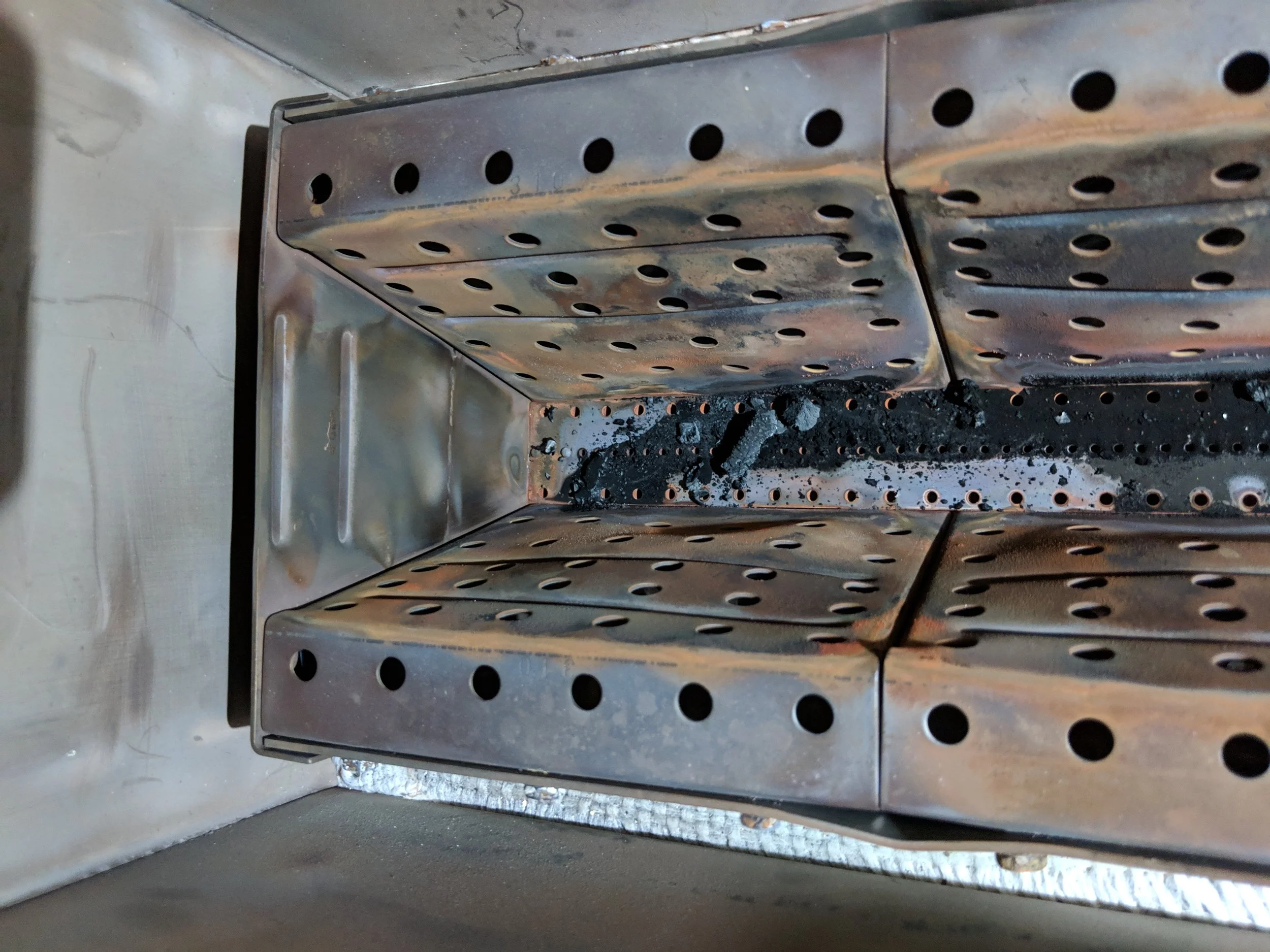 Stainless steel commercial oven with perforated trays and some burnt residue and debris inside.