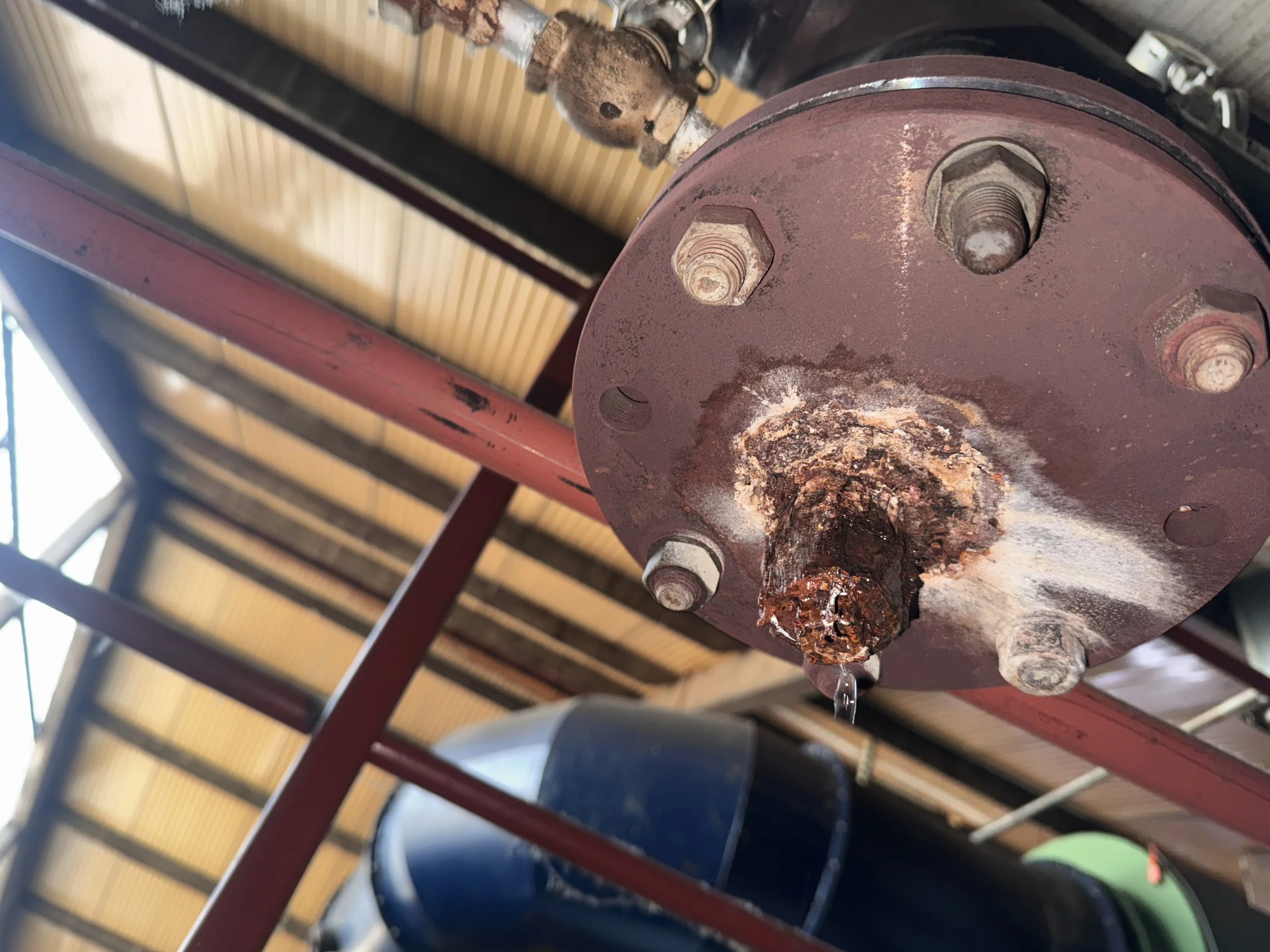 Close-up of a rusty metal component with bolts and water dripping from it, part of a larger mechanical or industrial structure.