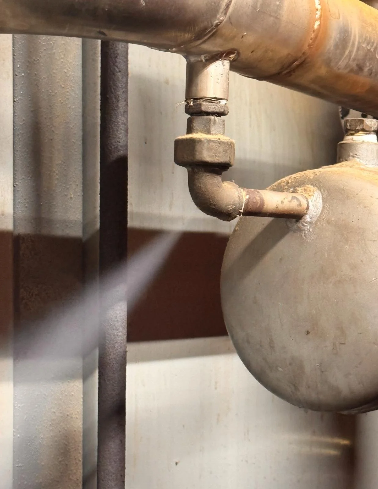 Close-up of a rusty water pipe connected to a large metal container or tank, with water flowing from the pipe.