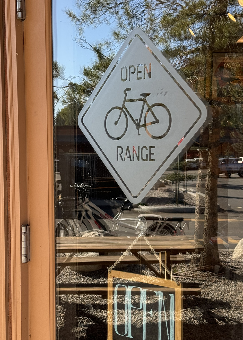 Glass door with a sign that says "Open" and an additional sign indicating bicycle range available outside.