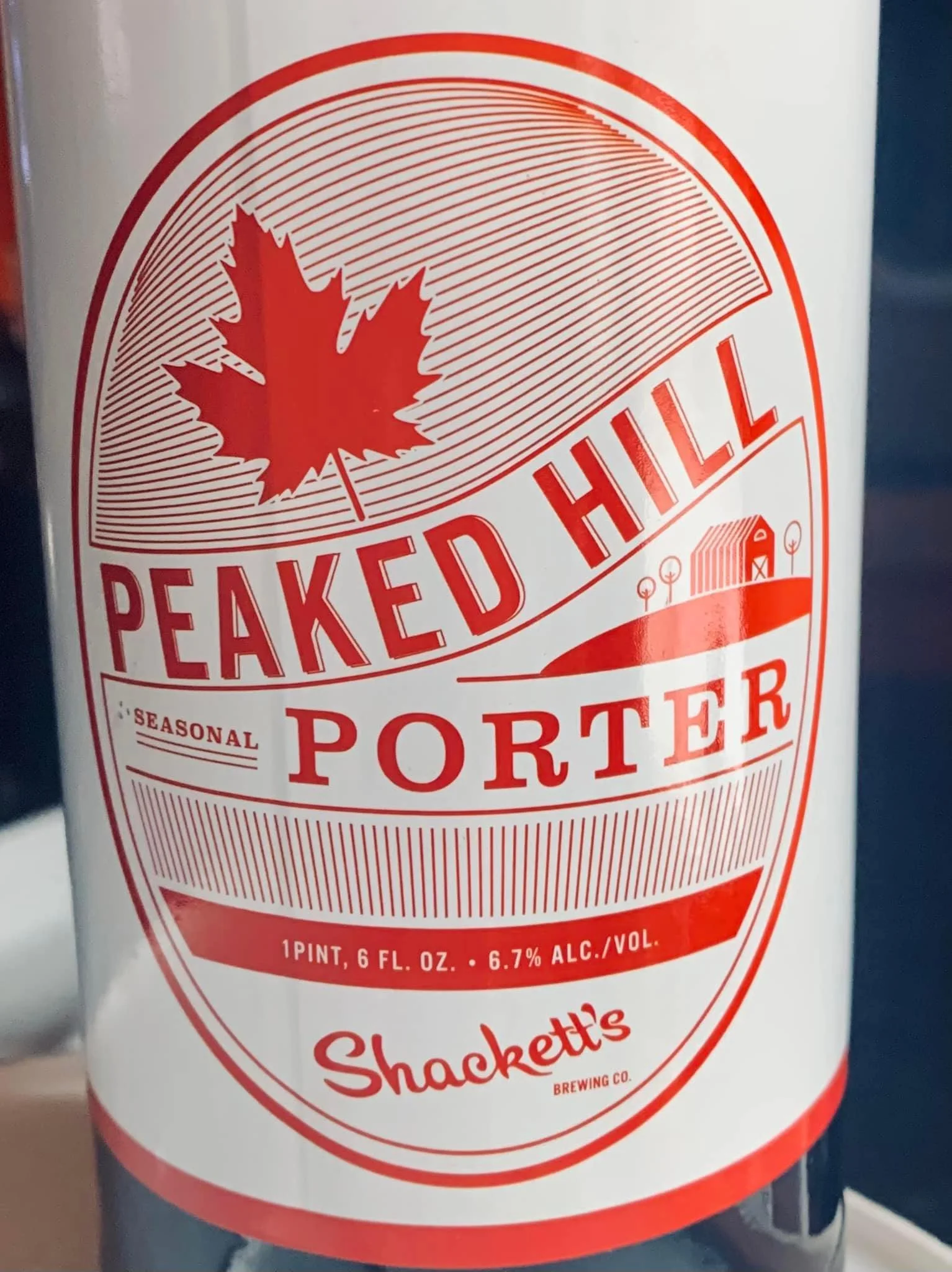 Label on a can of Peaked Hill Porter beer with a red maple leaf symbol and an illustration of a barn and landscape.